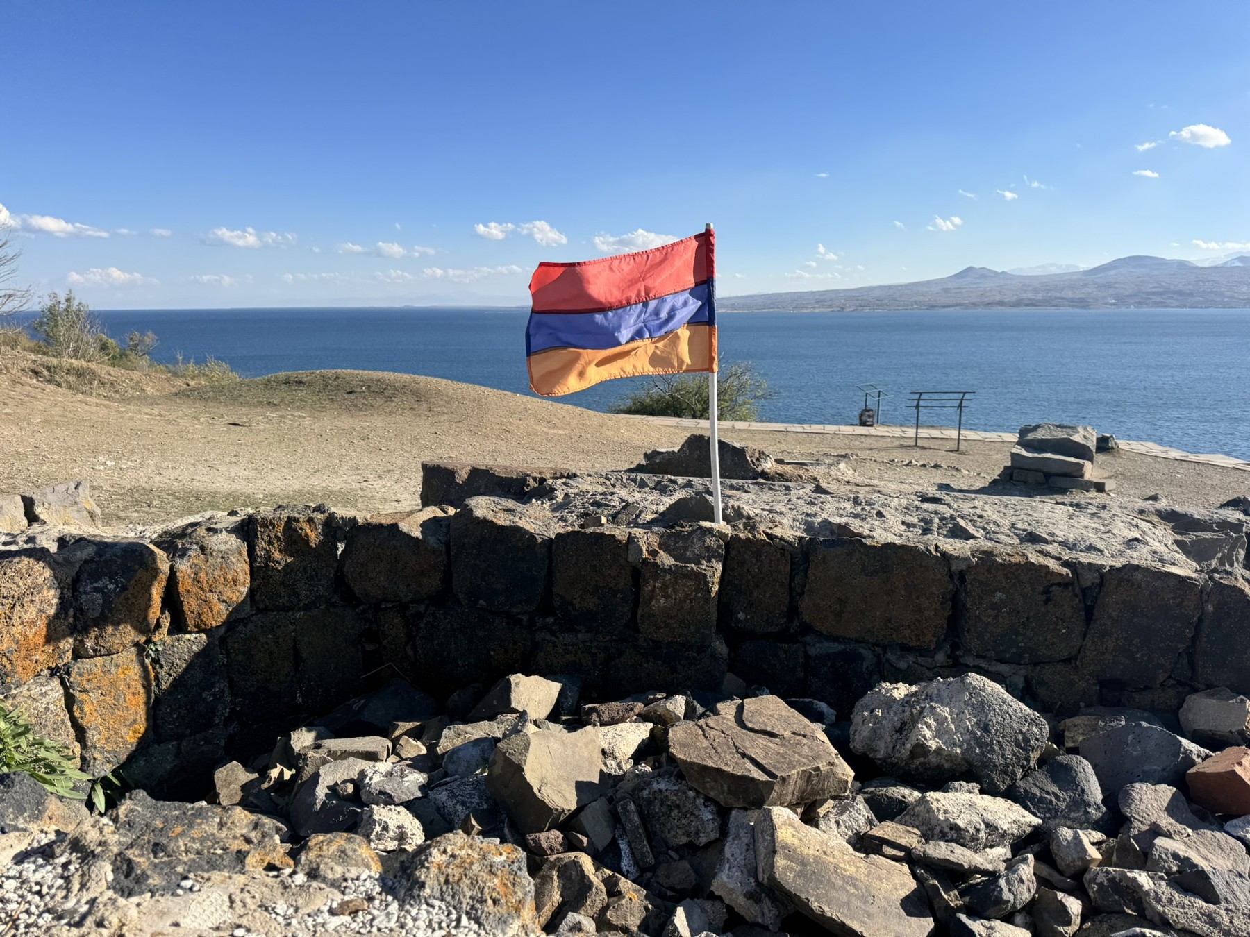 The Armenian flag above stone ruins overlooking blue Lake Sevan.