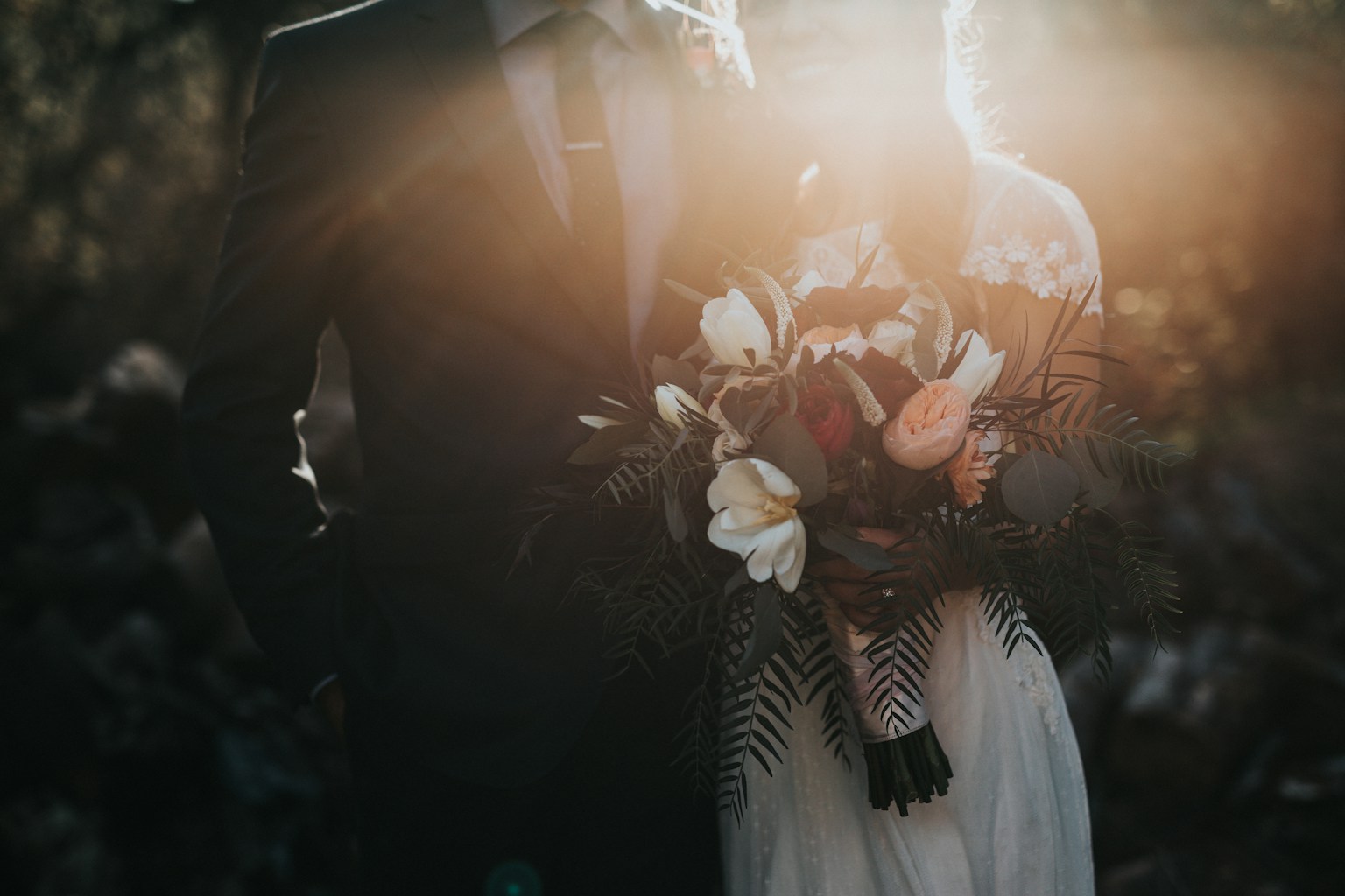 Couple standing close together with a bouquet in warm outdoor light
