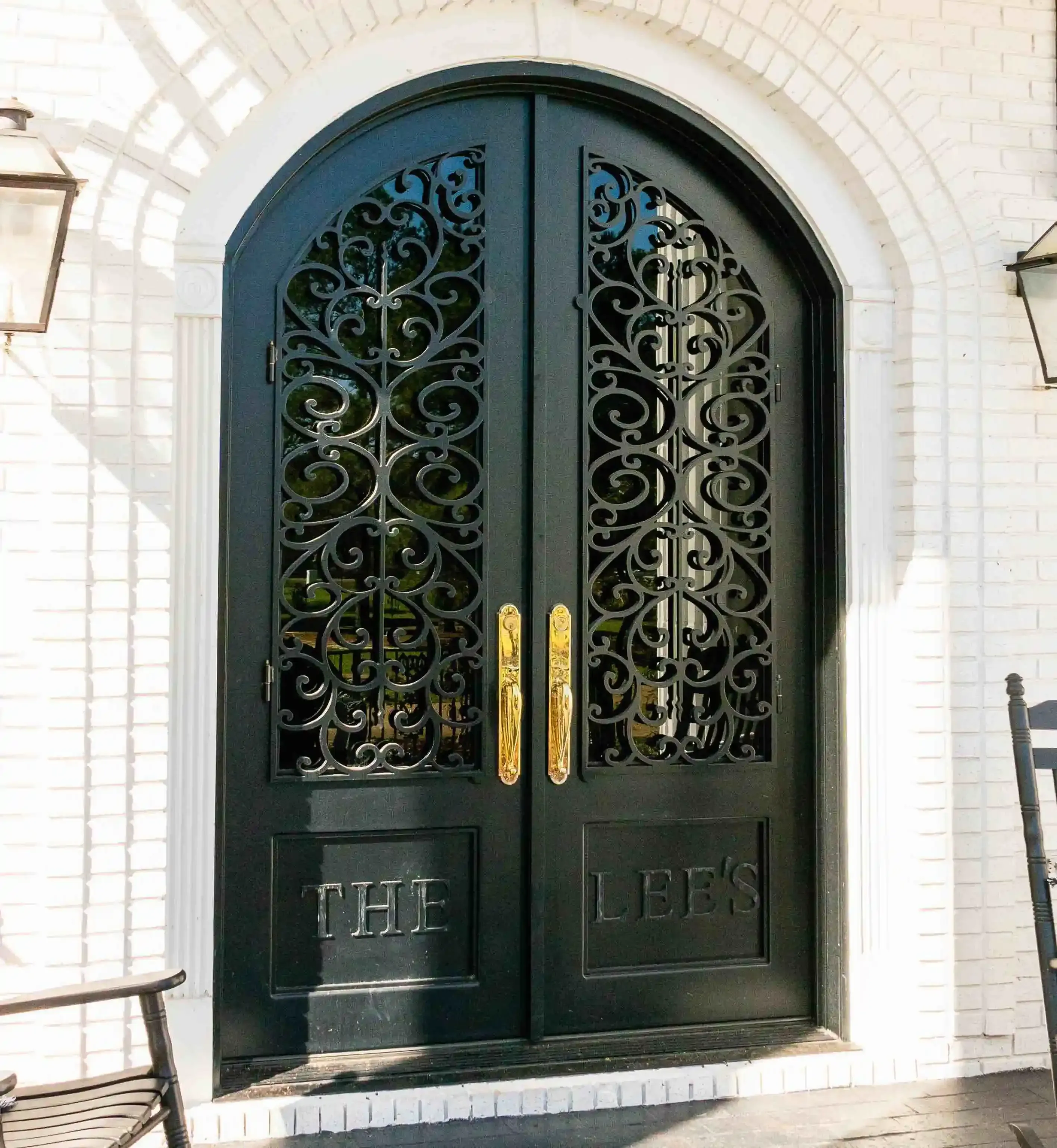 the front of a white home, in the middle there is a black iron door with large panes of glass on each door with intricate black iron swirls on each. The door is arched into a half circle at the top