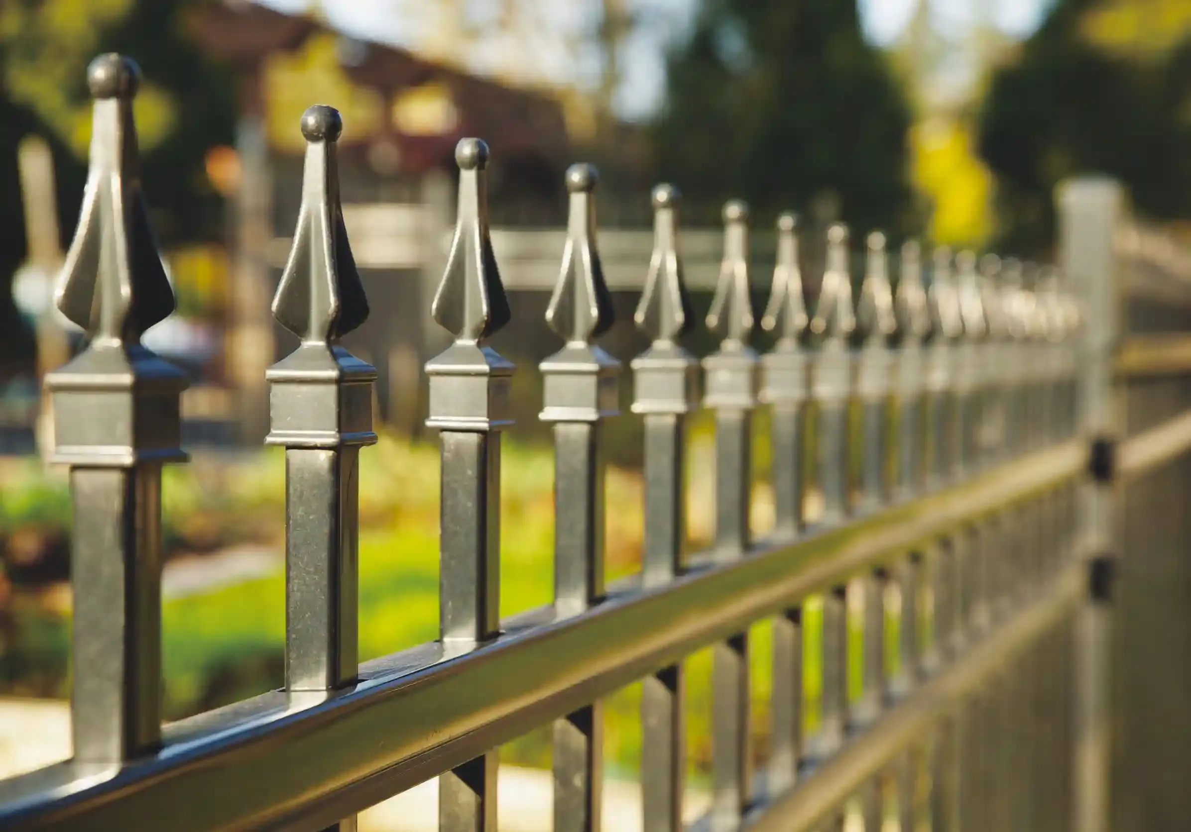 a black iron fence with ornate top and grass behind it