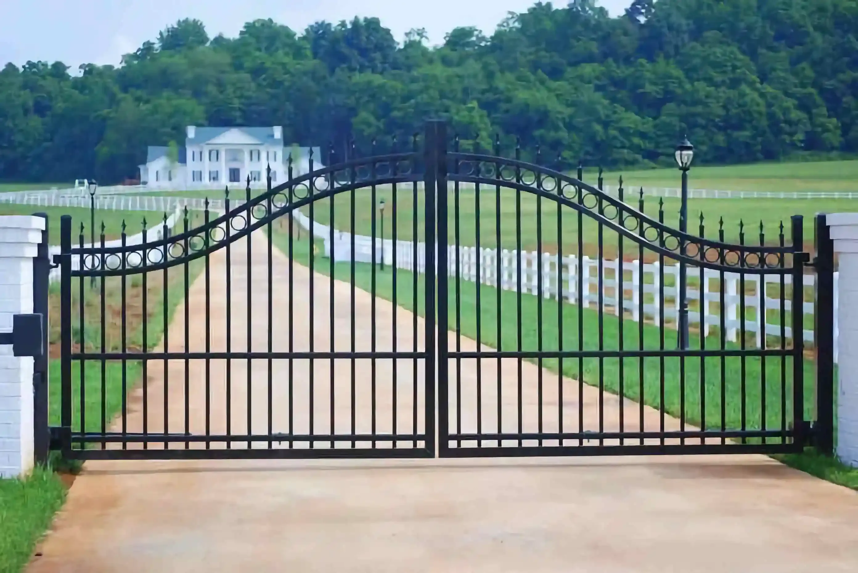 a large black iron gate in the middle of a long driveway leading to a home
