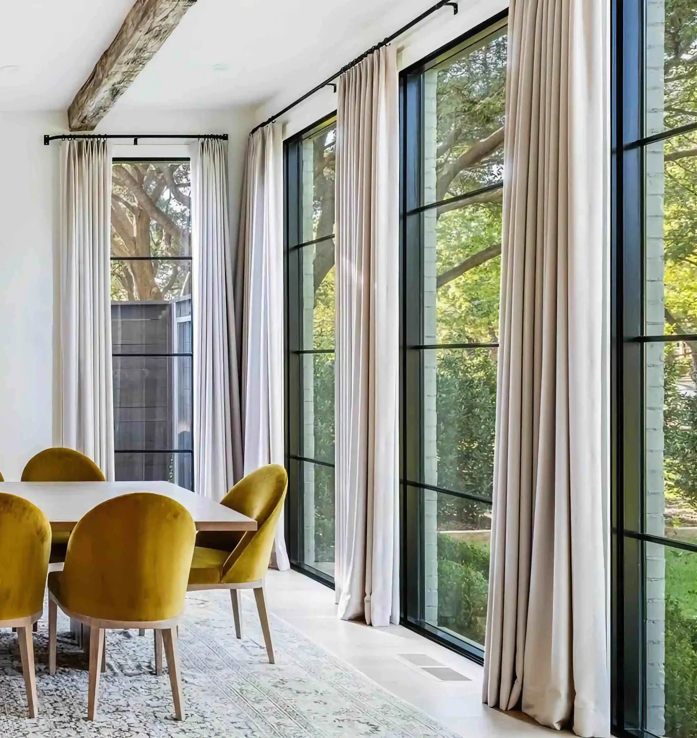 in a modern dining room with mustard colored chairs around a table and 4 floor to ceiling black iron and glass windows on the right side of the room