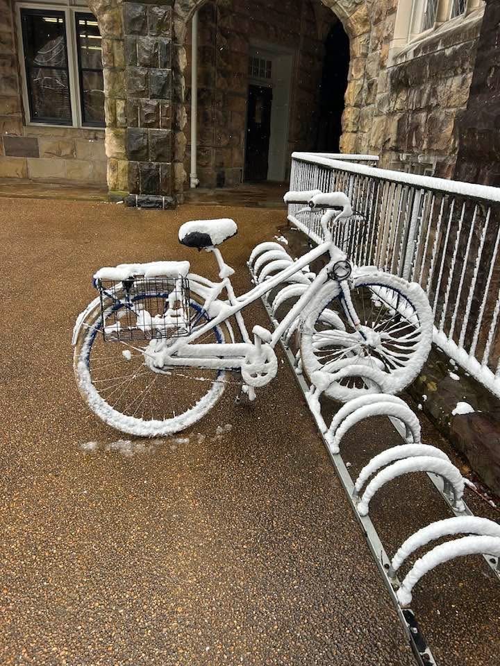 Snow-covered bicycle outside a stone building