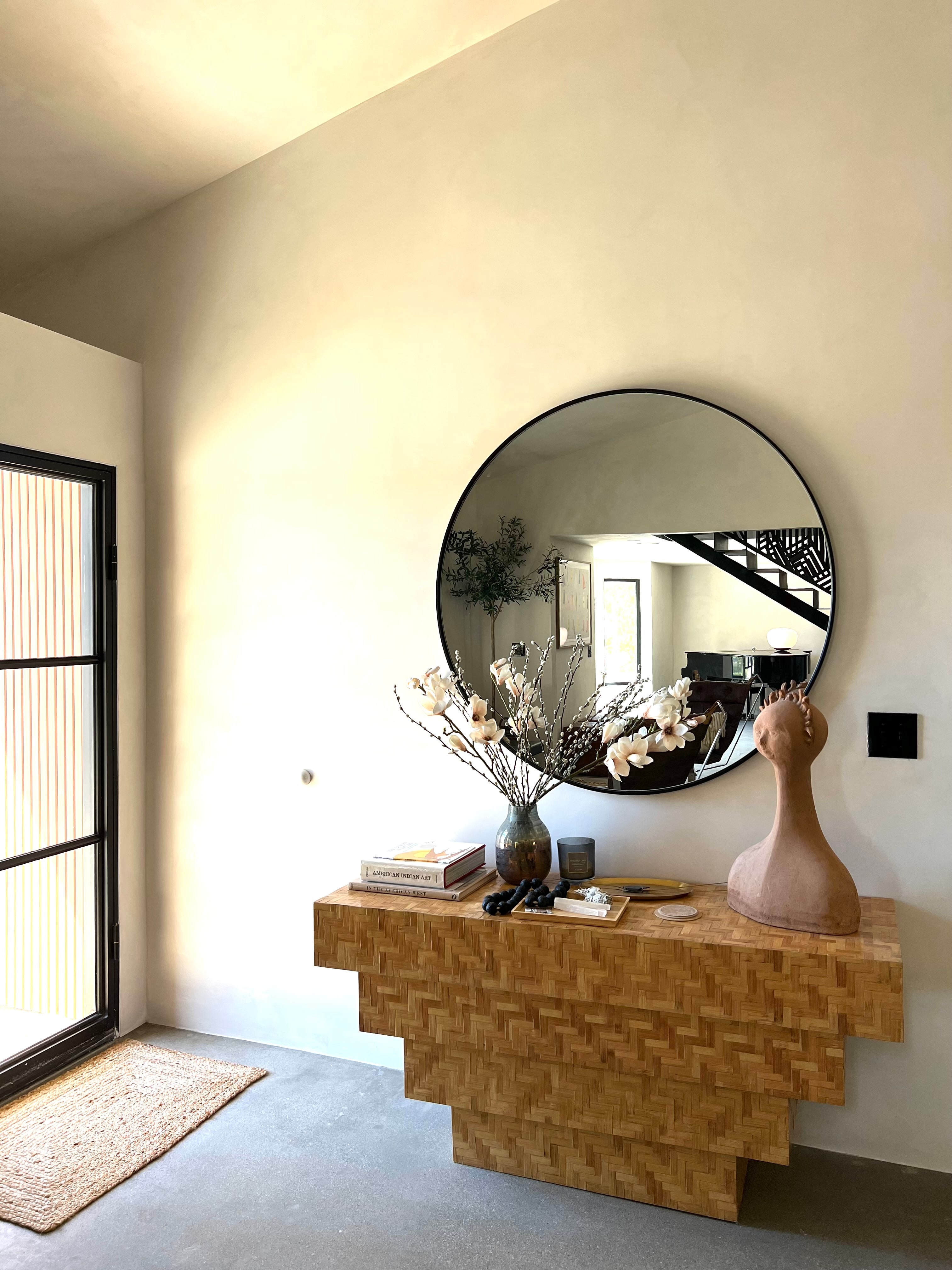 Sunlit entry with a large round mirror, sculptural vase, and wood console