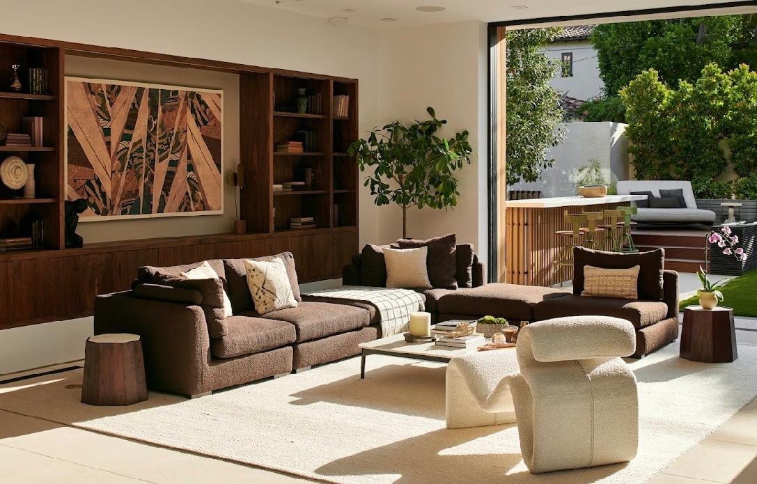 Sunlit living room with walnut shelving, deep brown seating, and an open garden terrace