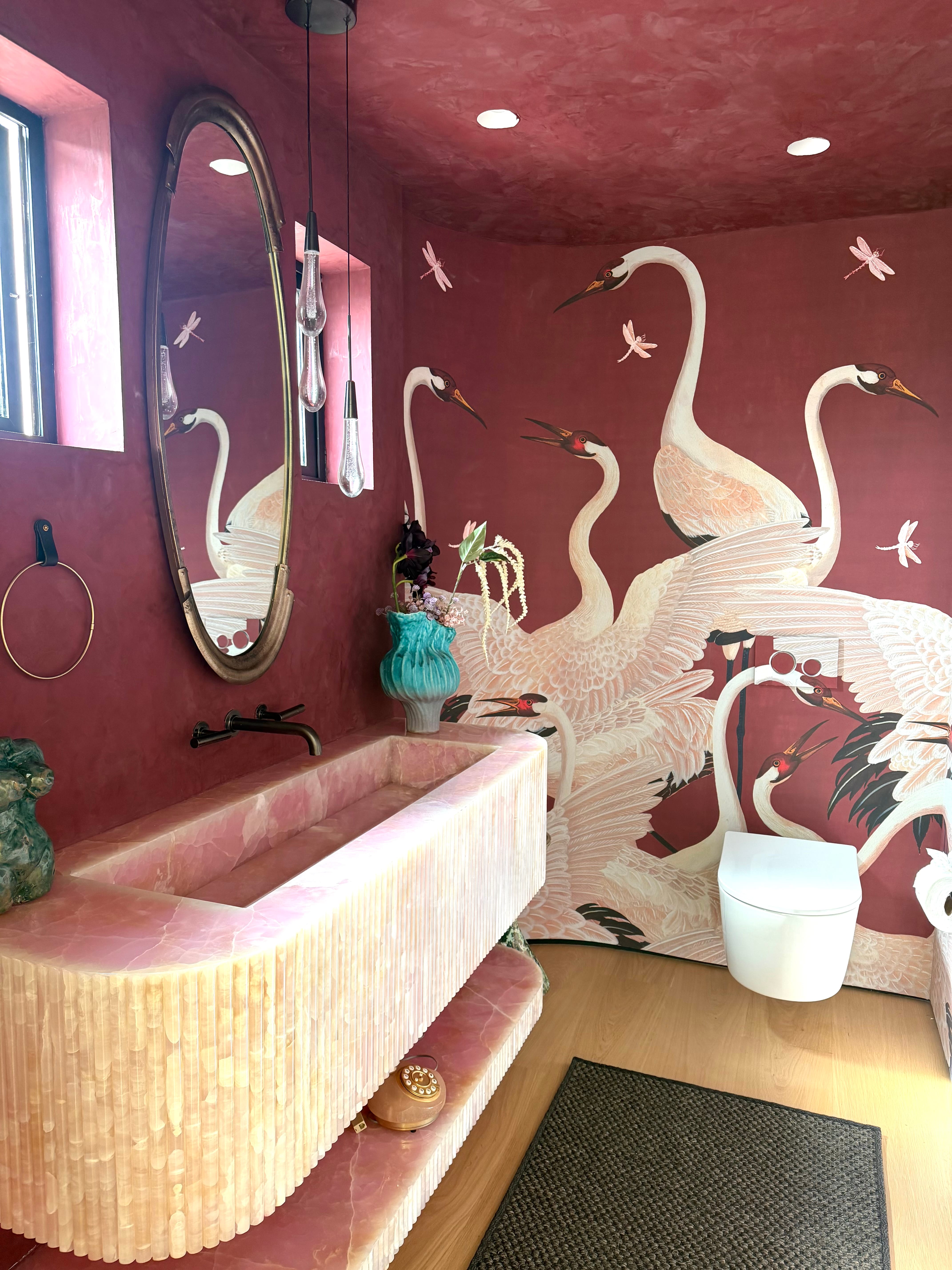 Pink onyx vanity with brass accents in a powder room with hand-painted crane mural walls