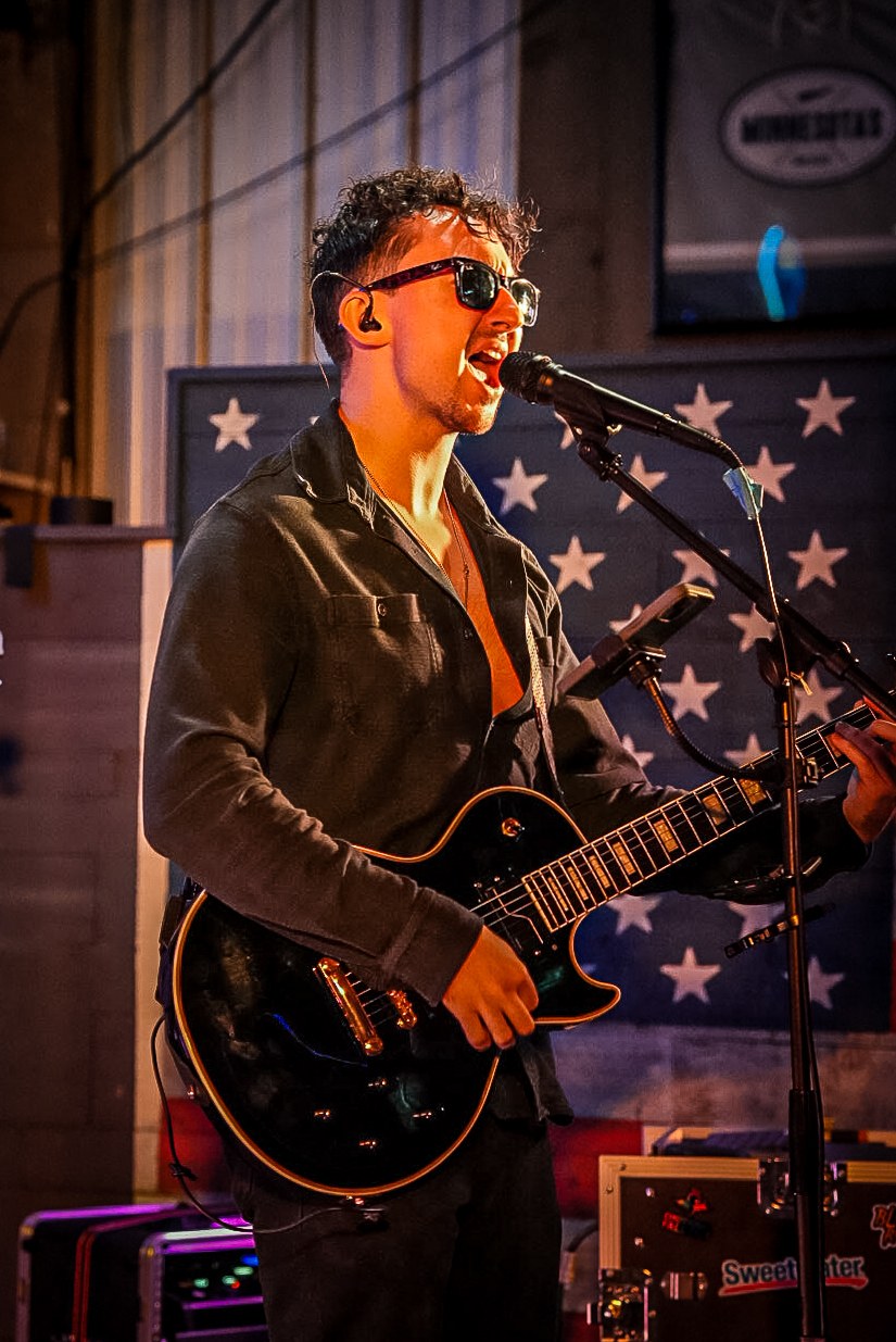 Guitarist singing and playing in front of an American flag