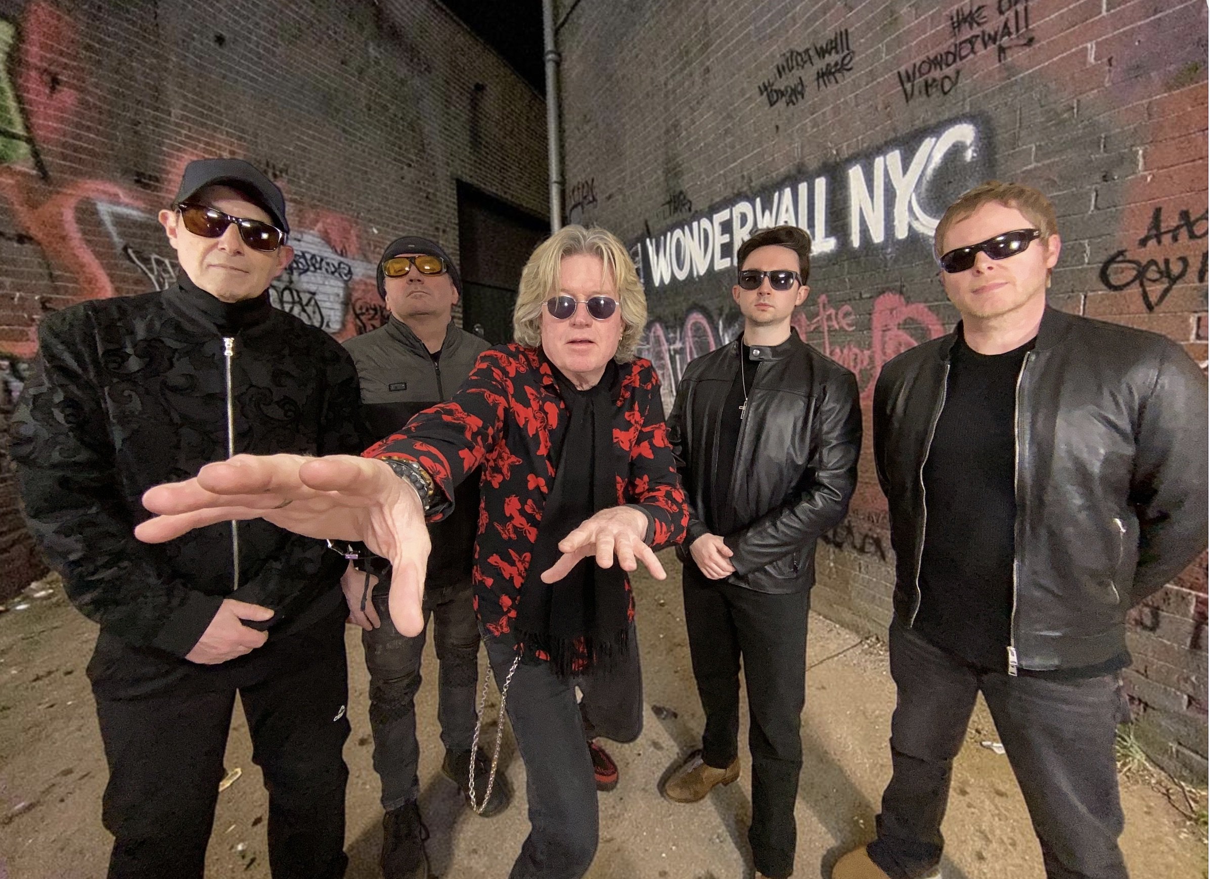 The five members of The Wonderwall beside a graffiti-covered brick wall