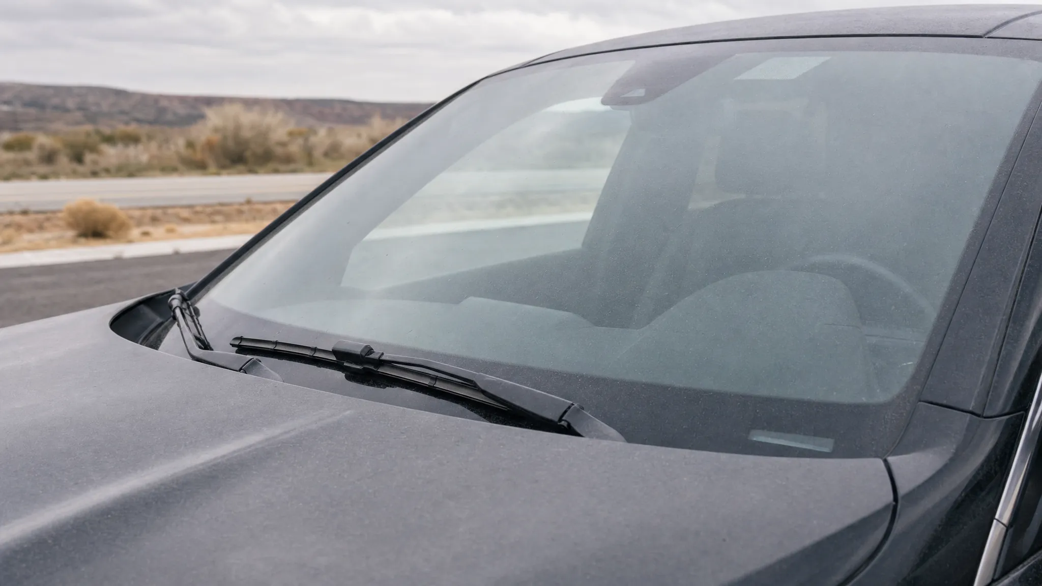 Close exterior view of a windshield and wiper blades after road driving