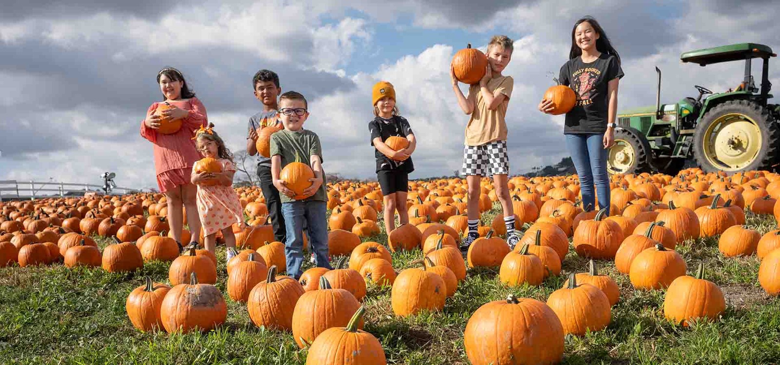 Children holding pumpkins in Cal Poly Pomona’s pumpkin field, with a tractor behind them