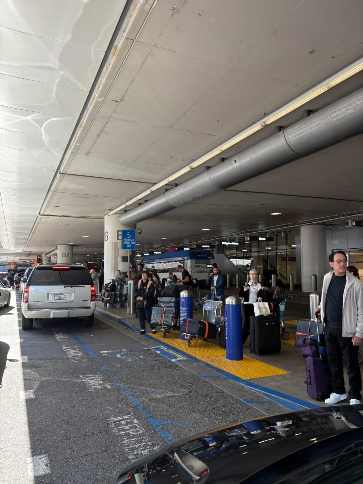 Real LAX arrivals curb with travelers, luggage carts, traffic and a shuttle bus