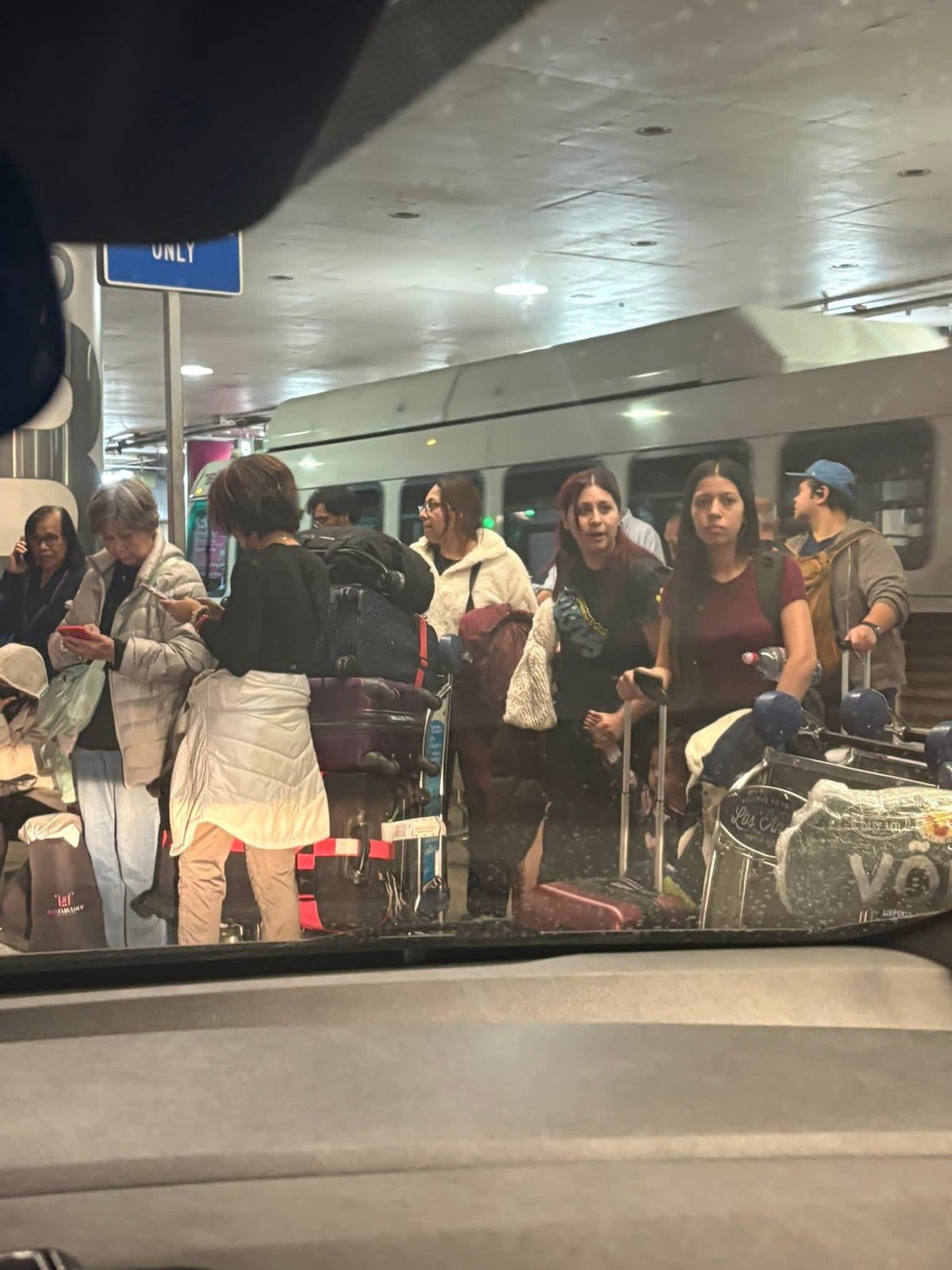 Travelers waiting with suitcases and luggage carts beside a shuttle at LAX