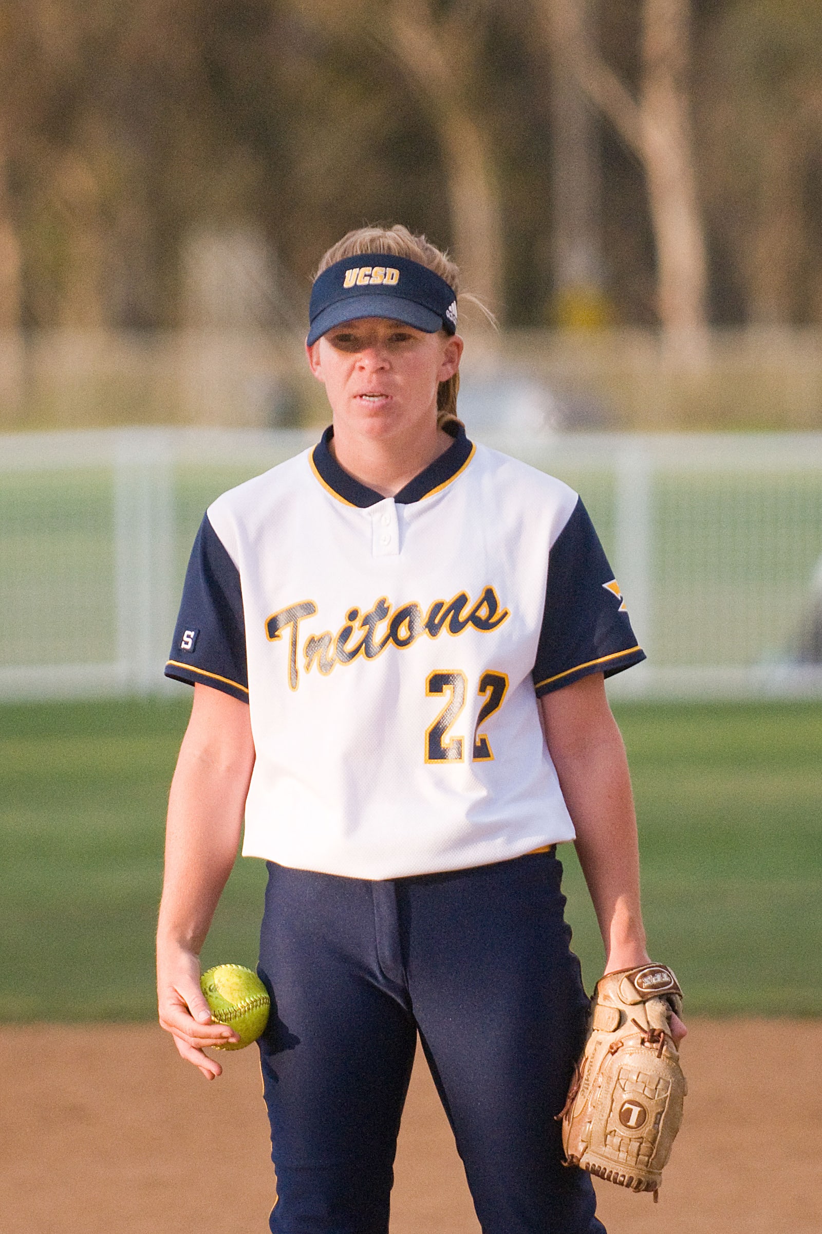 Softball pitcher standing on the field holding a ball and glove