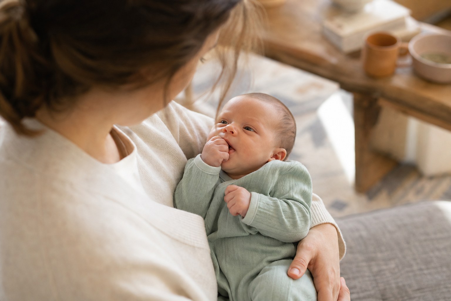 An alert newborn bringing a hand toward their mouth while held by a parent
