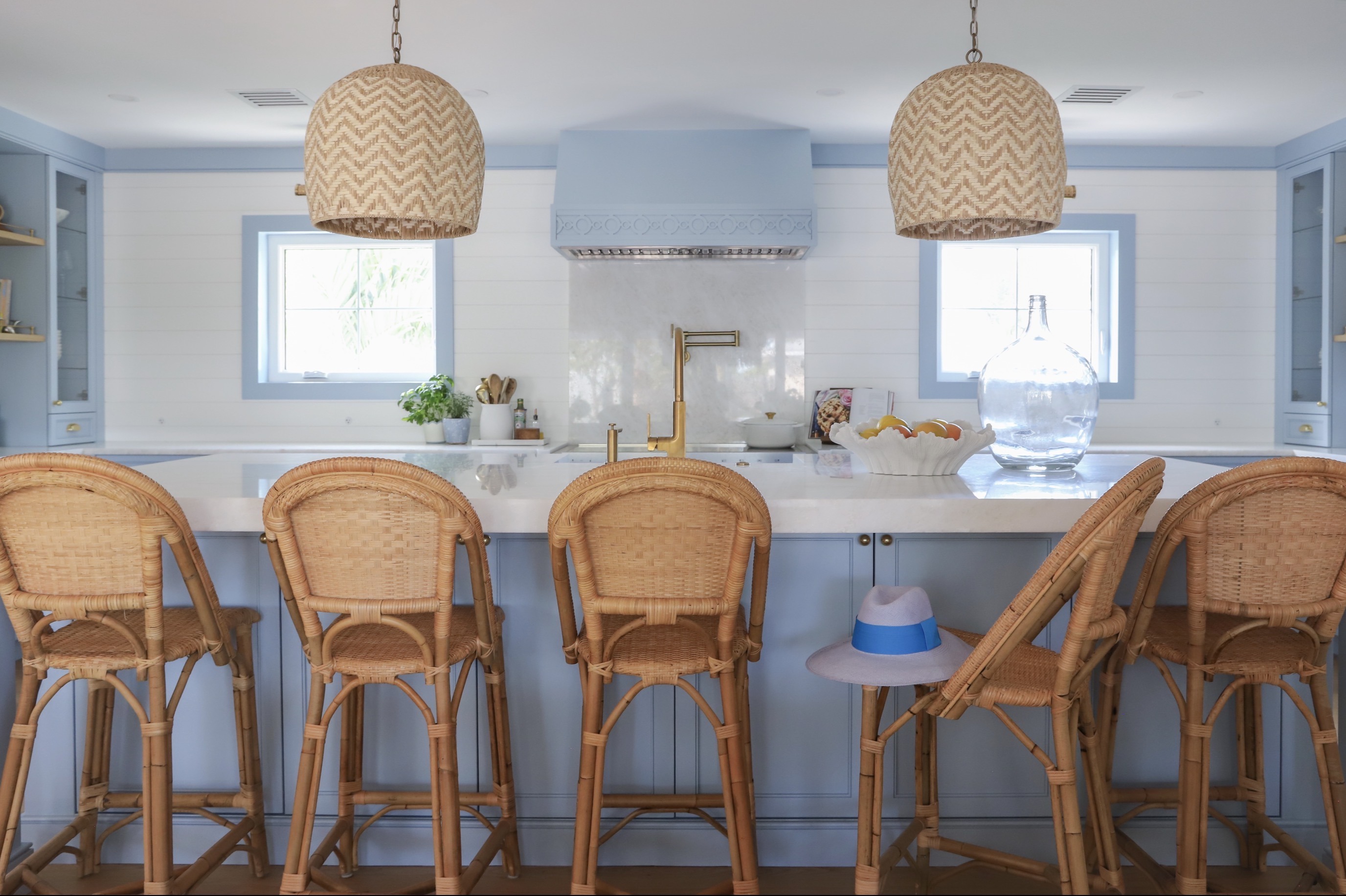Blue custom kitchen cabinetry with a marble island and woven counter stools