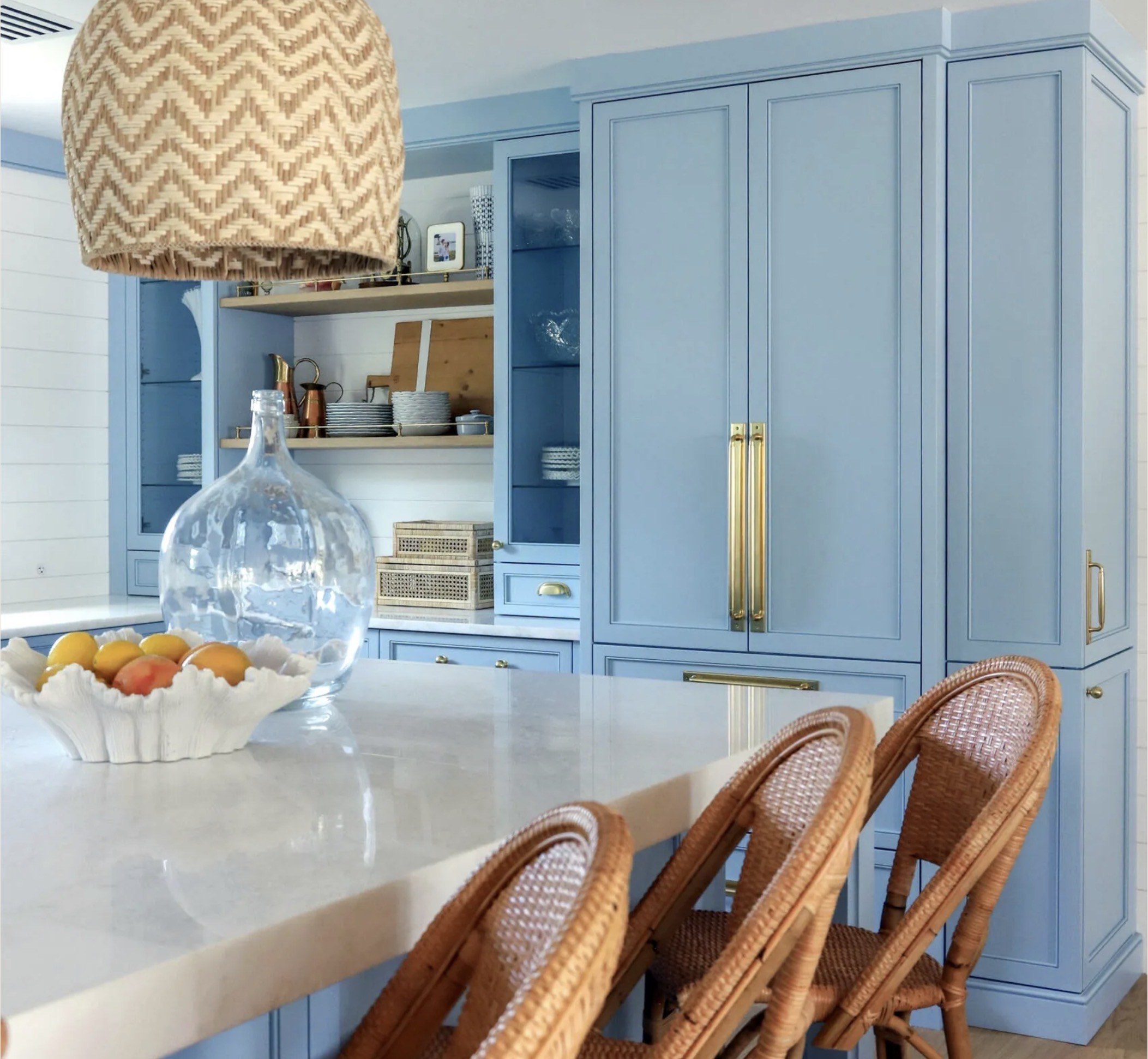 Blue custom kitchen cabinetry with a marble island, brass hardware and woven counter stools