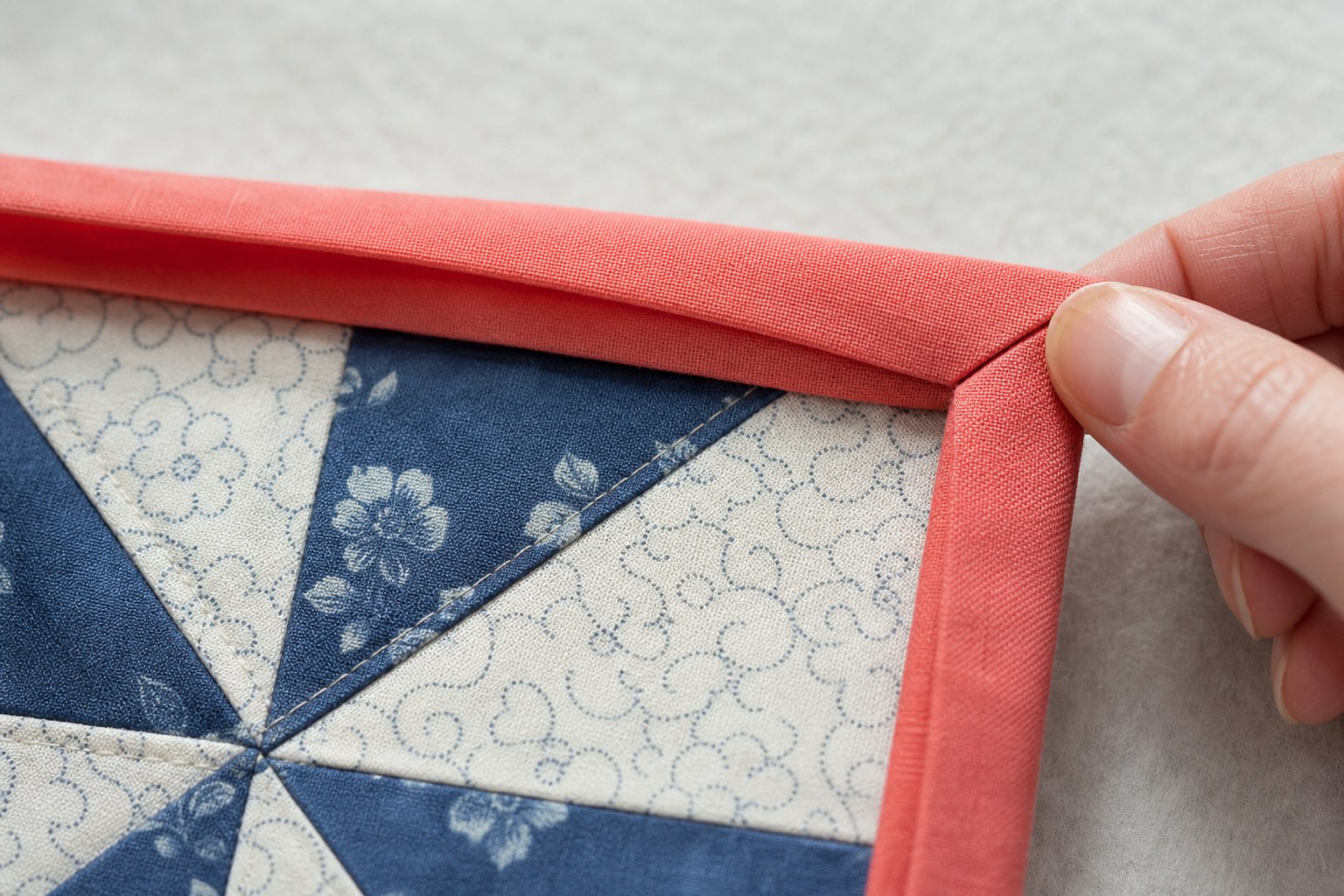 Crisp coral mitered binding folded around a square patchwork quilt corner