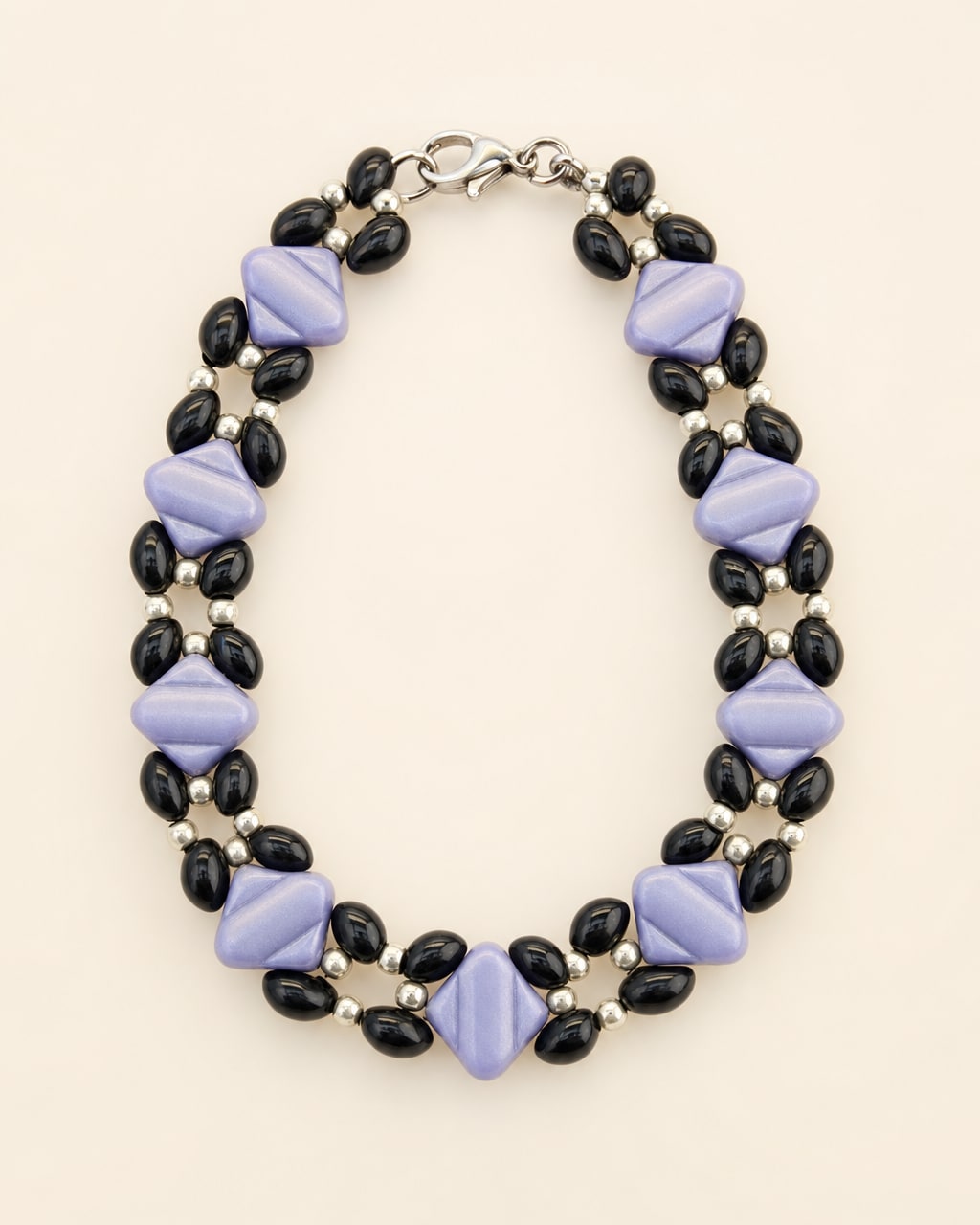 Lavender and black beaded bracelet arranged on a warm ivory studio background