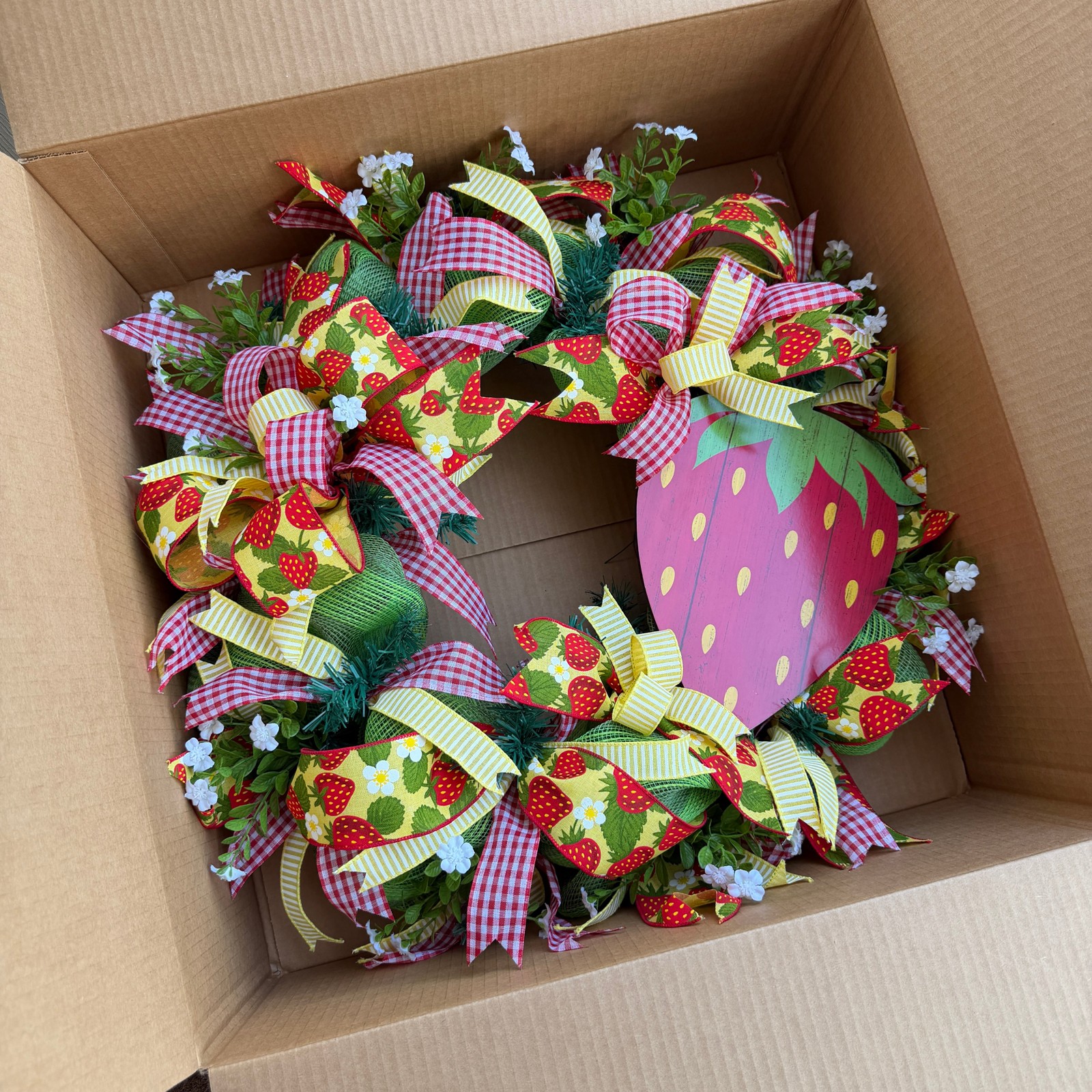 Joan’s strawberry wreath with gingham and strawberry ribbons resting in a cardboard box
