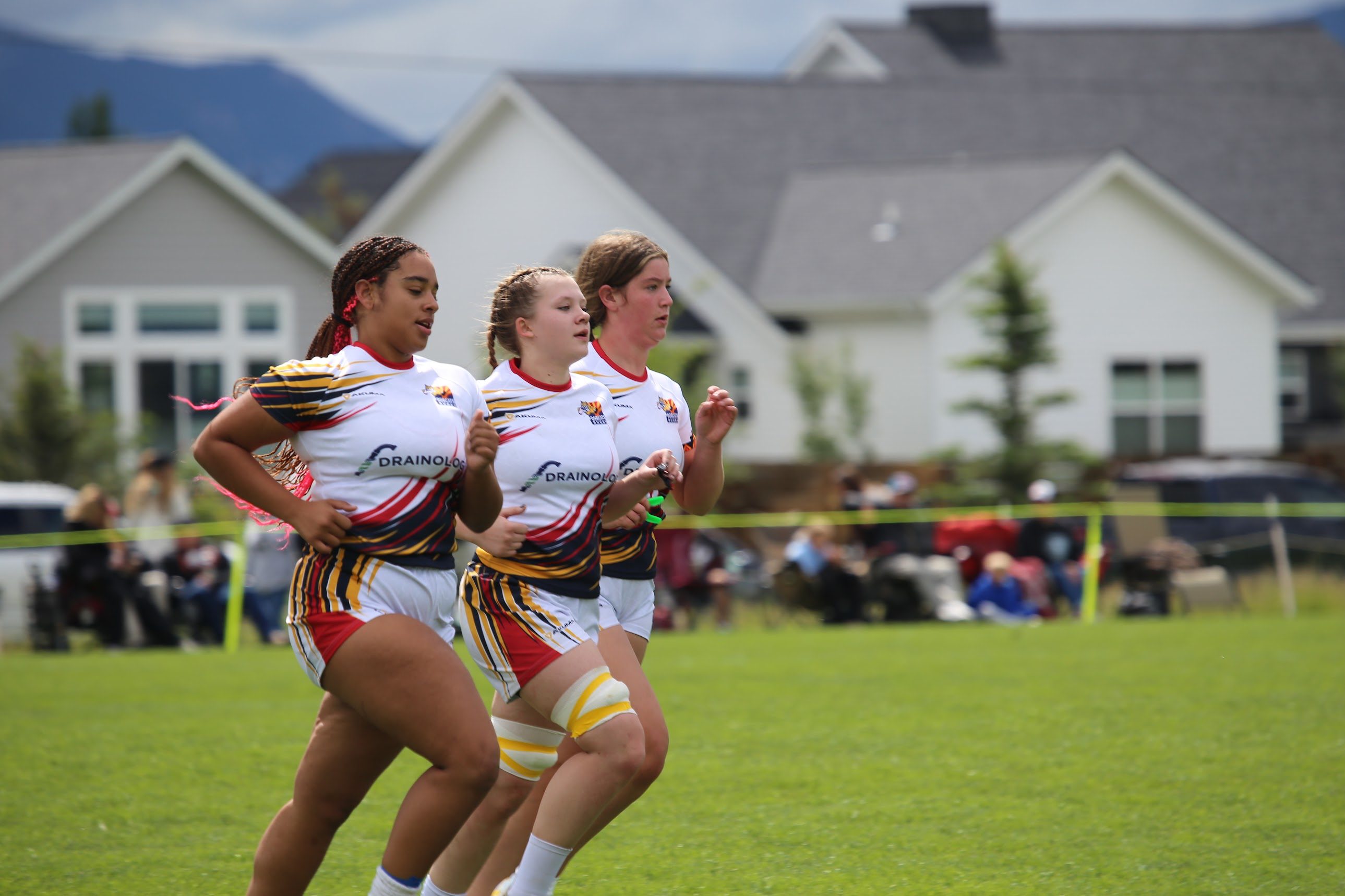 Three Bobcats girls rugby players running together on the field