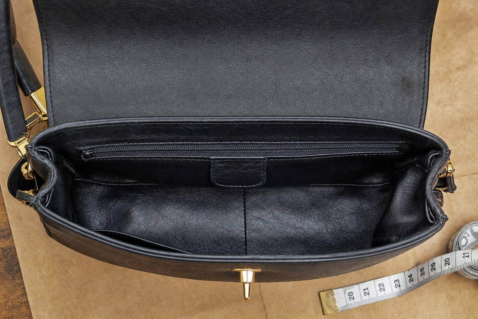 Open anonymous black leather handbag showing its lining, interior pocket, and zipper