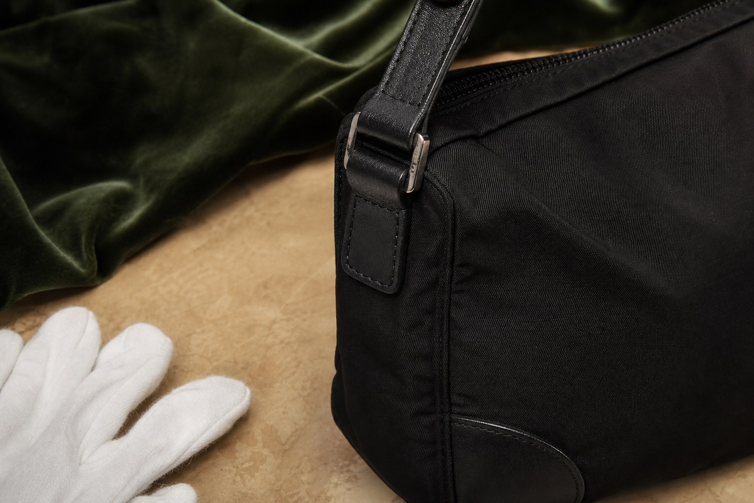 Close view of an unbranded black nylon bag's zipper, strap attachment, and leather corner