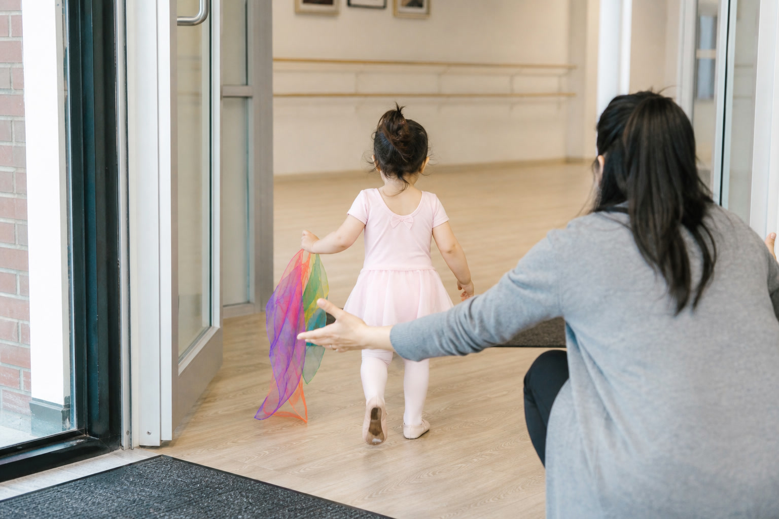 A toddler walking into a dance studio while a parent waits nearby