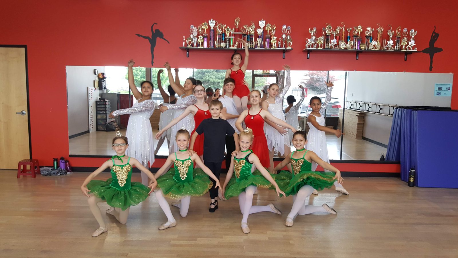 Ballet students posing together in green, red, and white costumes