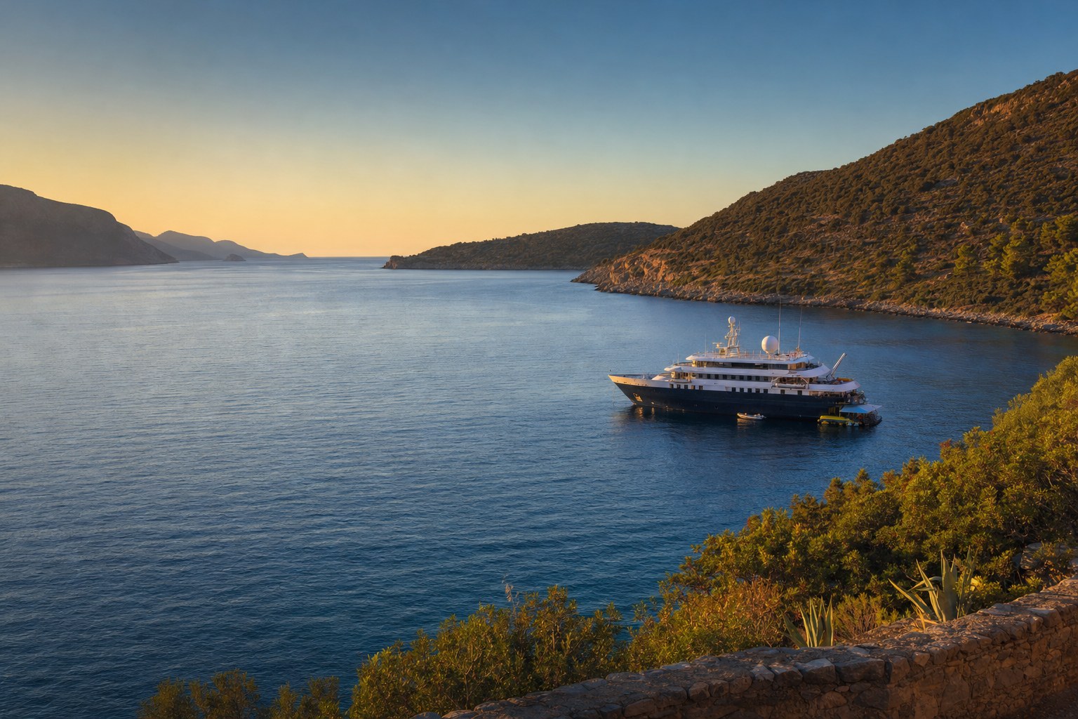 A small luxury cruise ship anchored in a Mediterranean cove at golden hour.