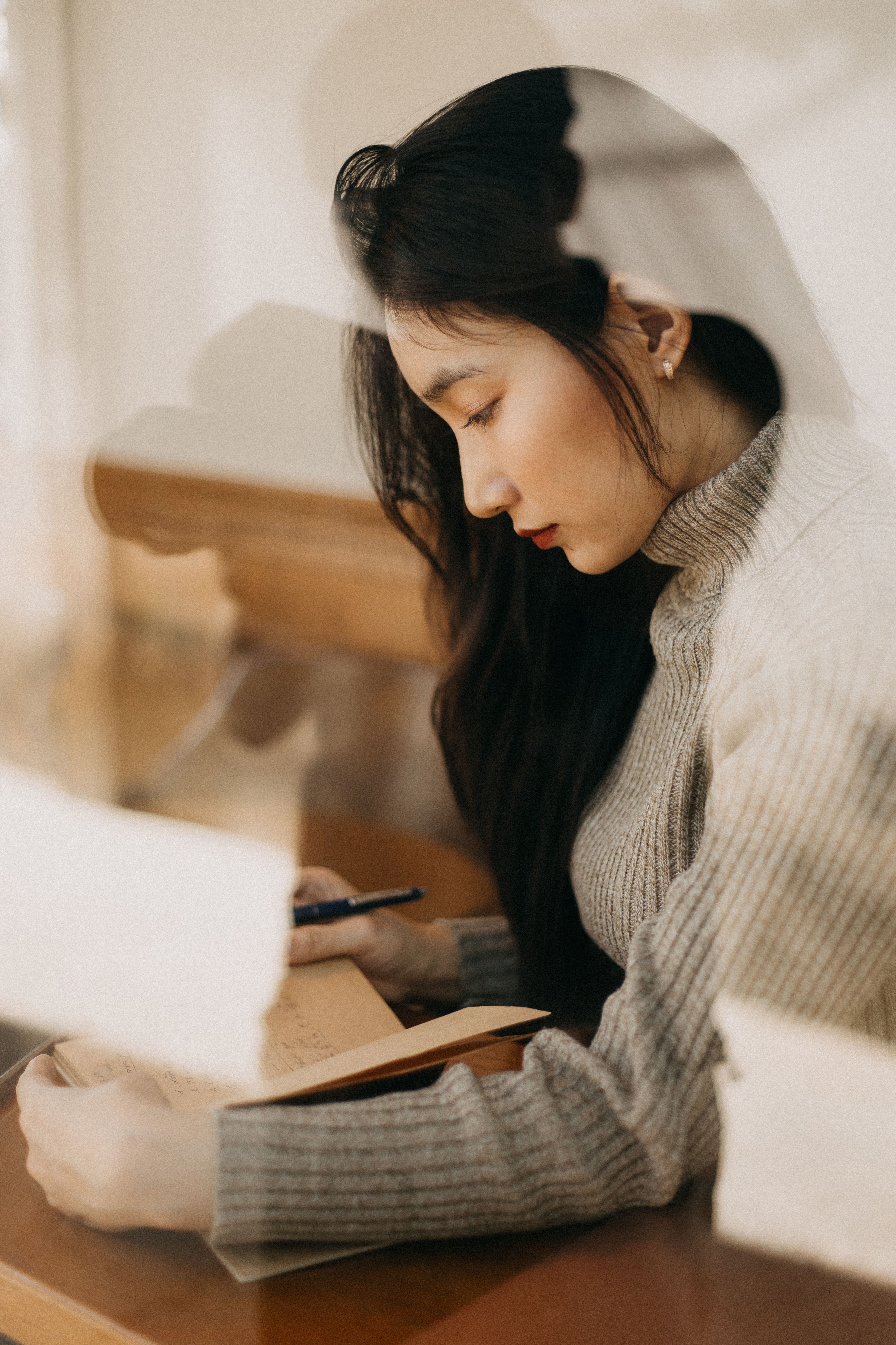 A woman writing in a journal near a window.