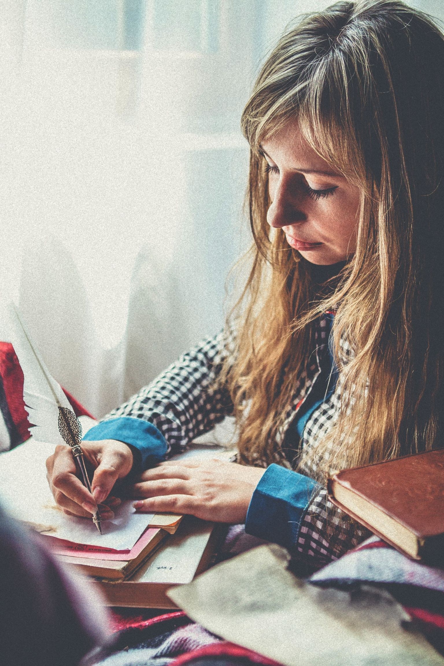 A woman writing quietly in a journal near a window.