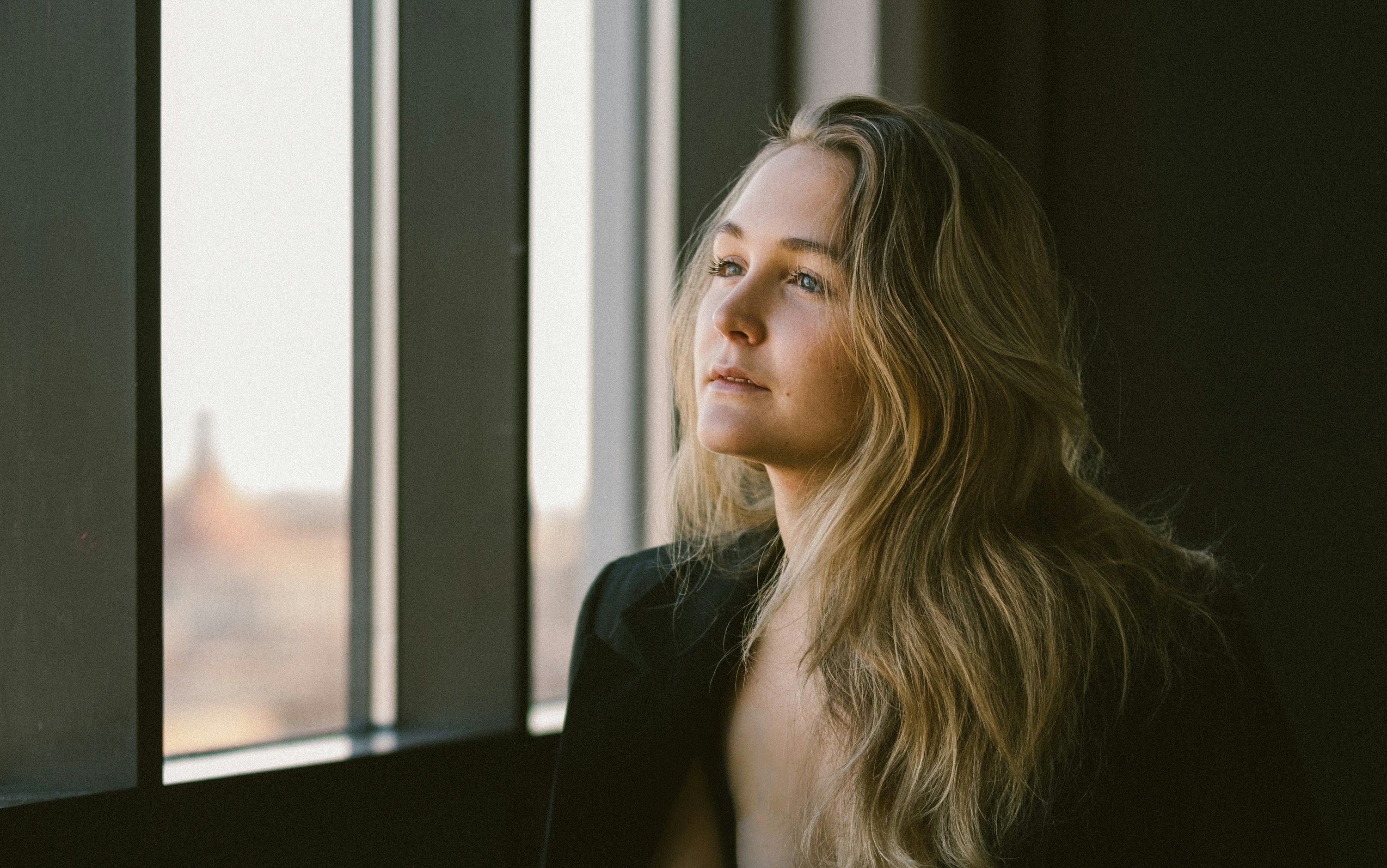 A woman sitting thoughtfully beside a window.