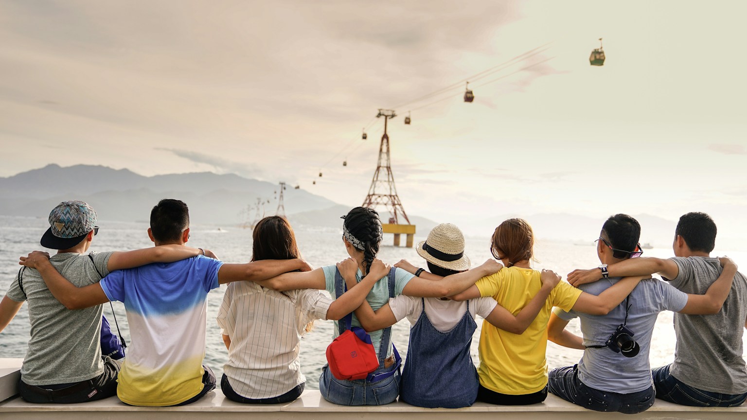 A group of friends sitting together with their arms around one another by the water.