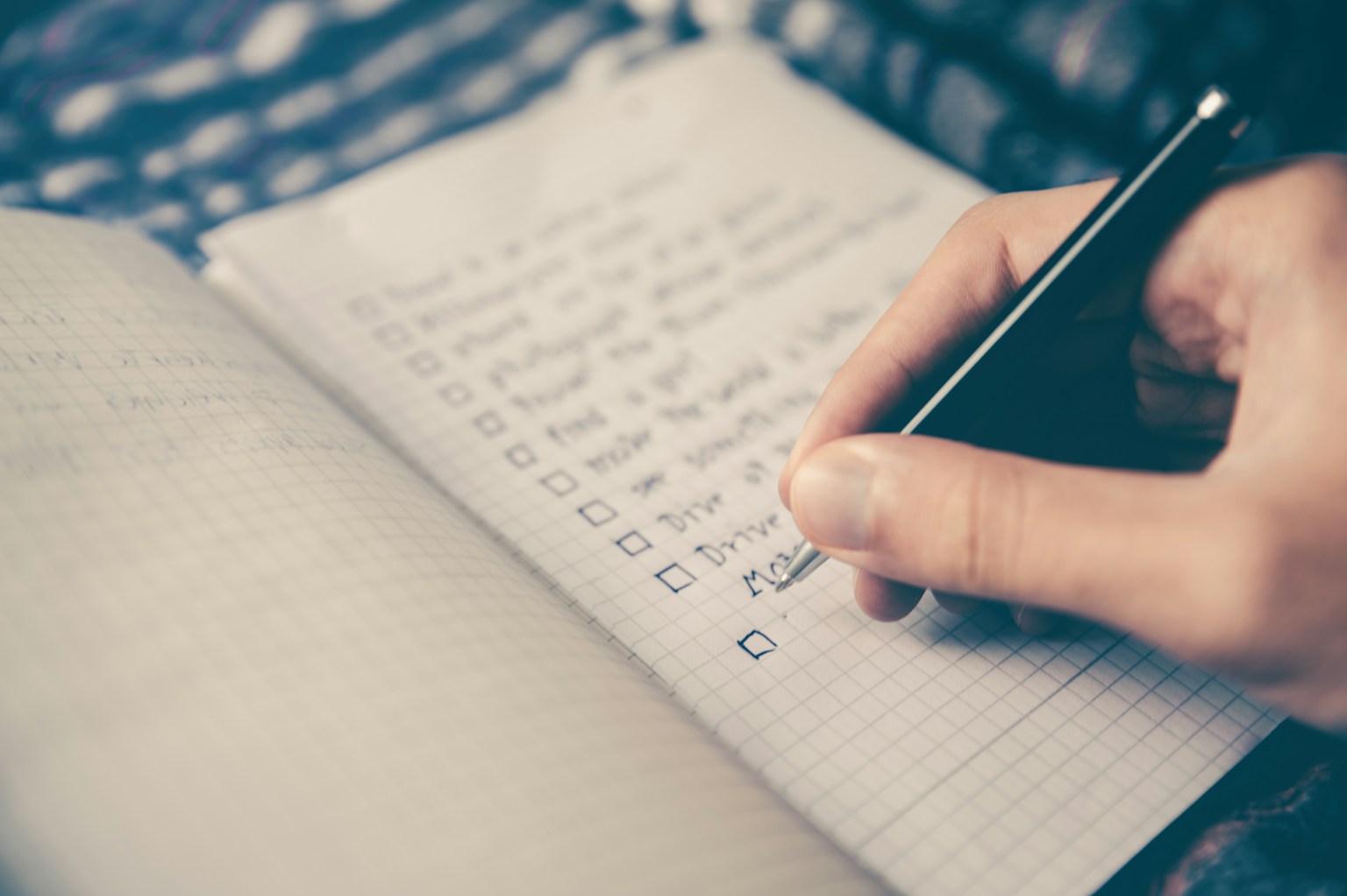 A hand writing in a grid notebook with a pen.