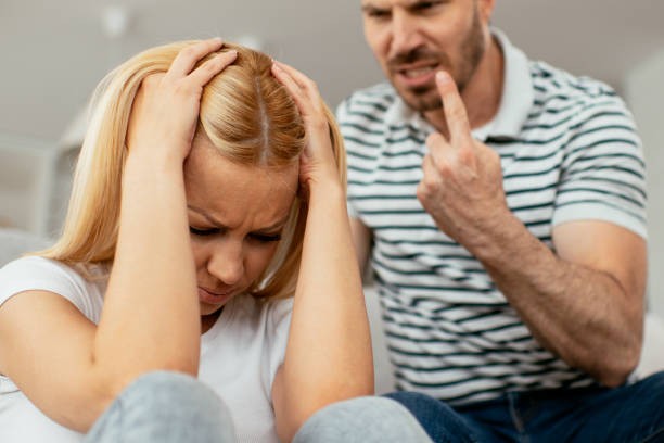 A distressed woman sitting beside a partner who is speaking angrily