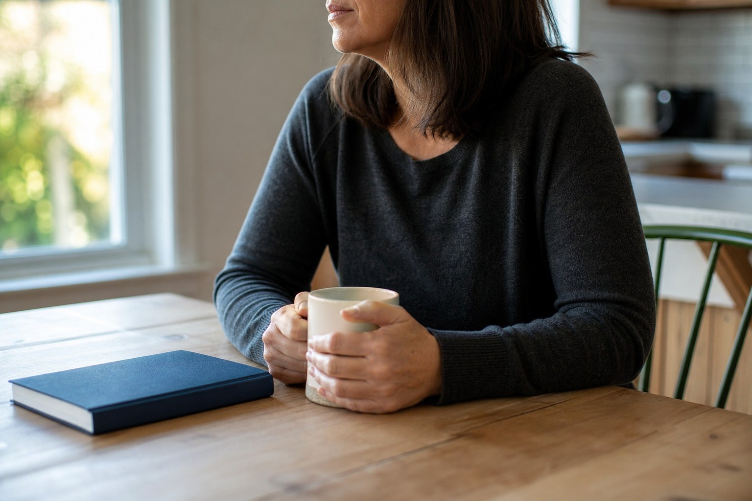A person taking a quiet pause with a warm mug at a kitchen table.