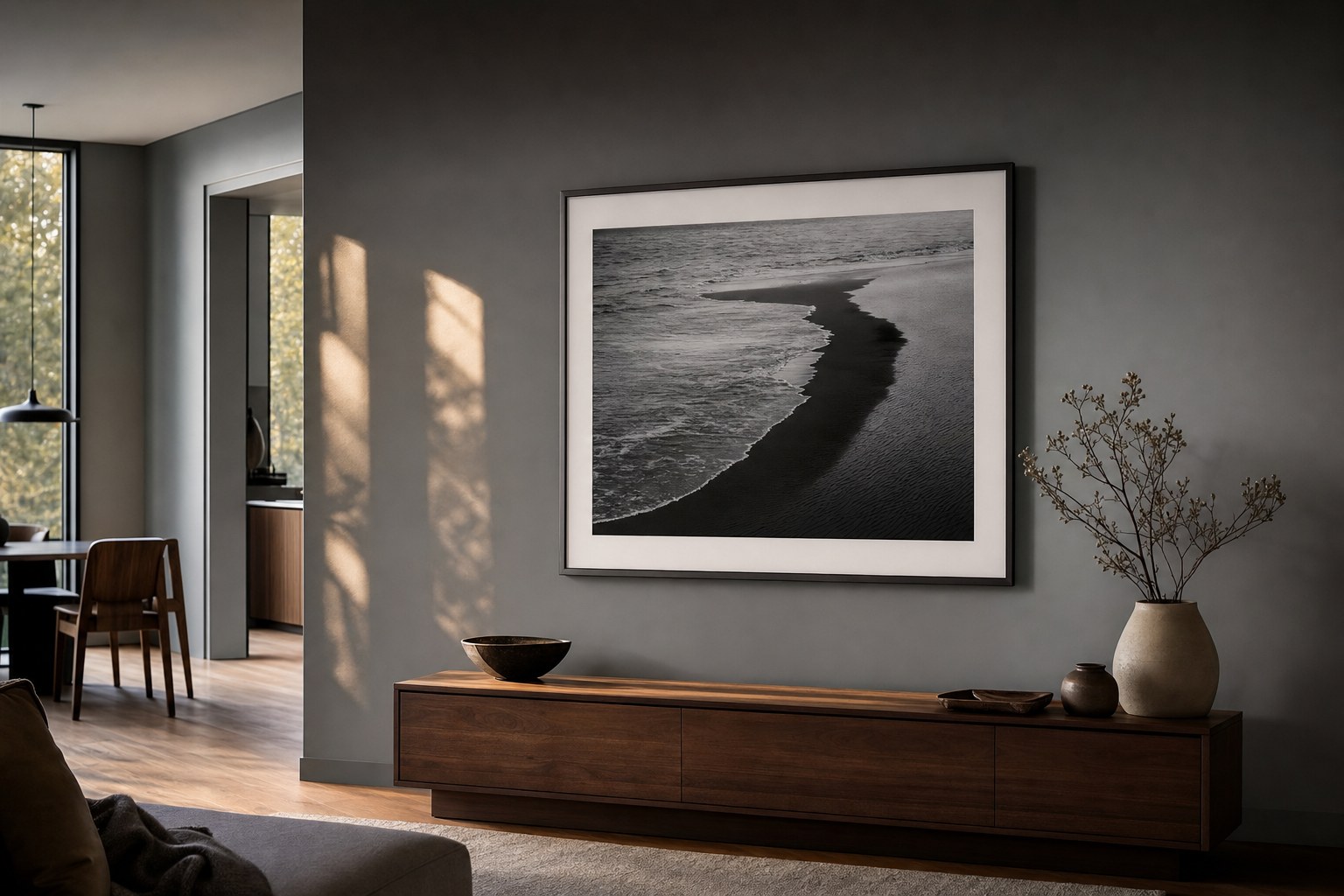 A framed black-and-white shoreline photograph displayed above a walnut console in a home.