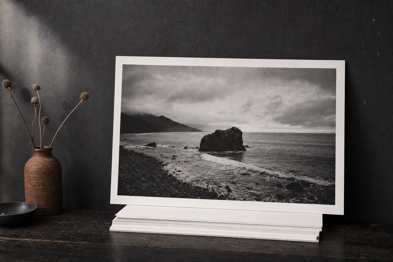 A black-and-white coastal photograph displayed as a large archival art print in a dark studio.
