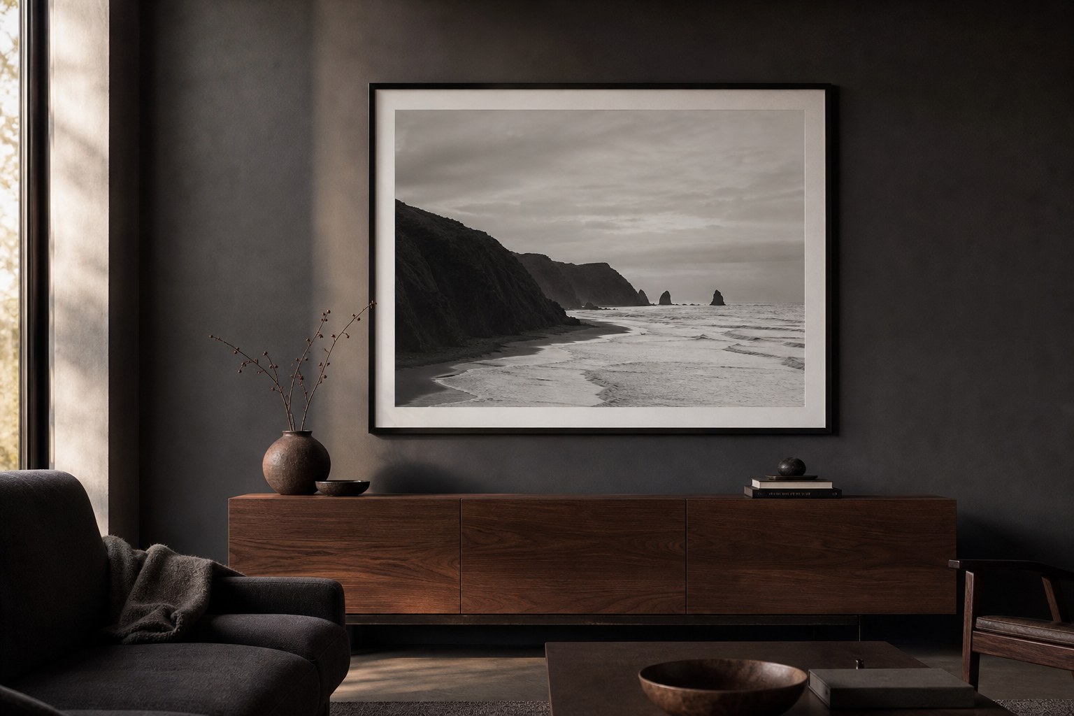 A framed black-and-white coastal photograph above a walnut console in a dark living room.