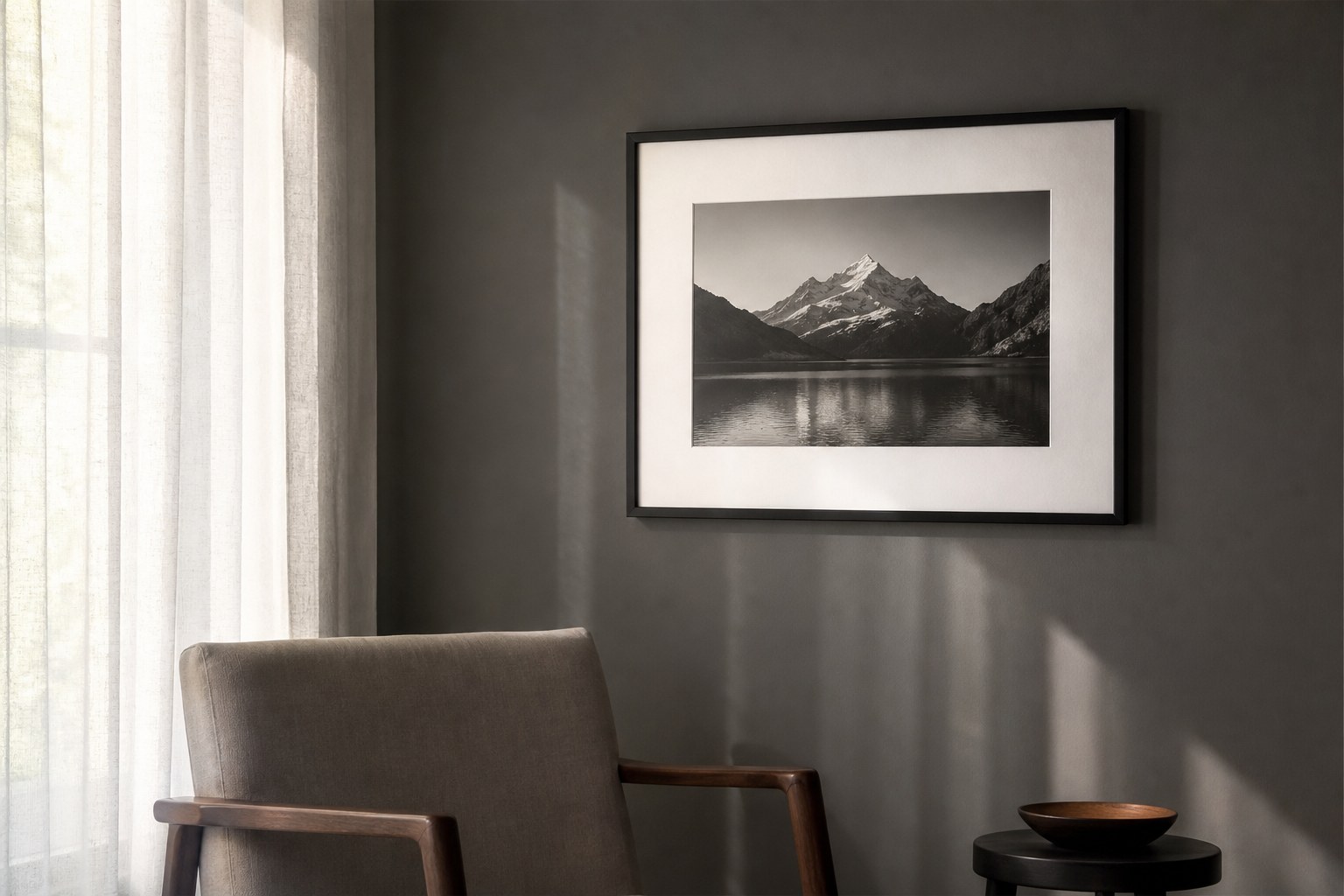 A framed monochrome photograph receiving soft indirect light beside sheer curtains.