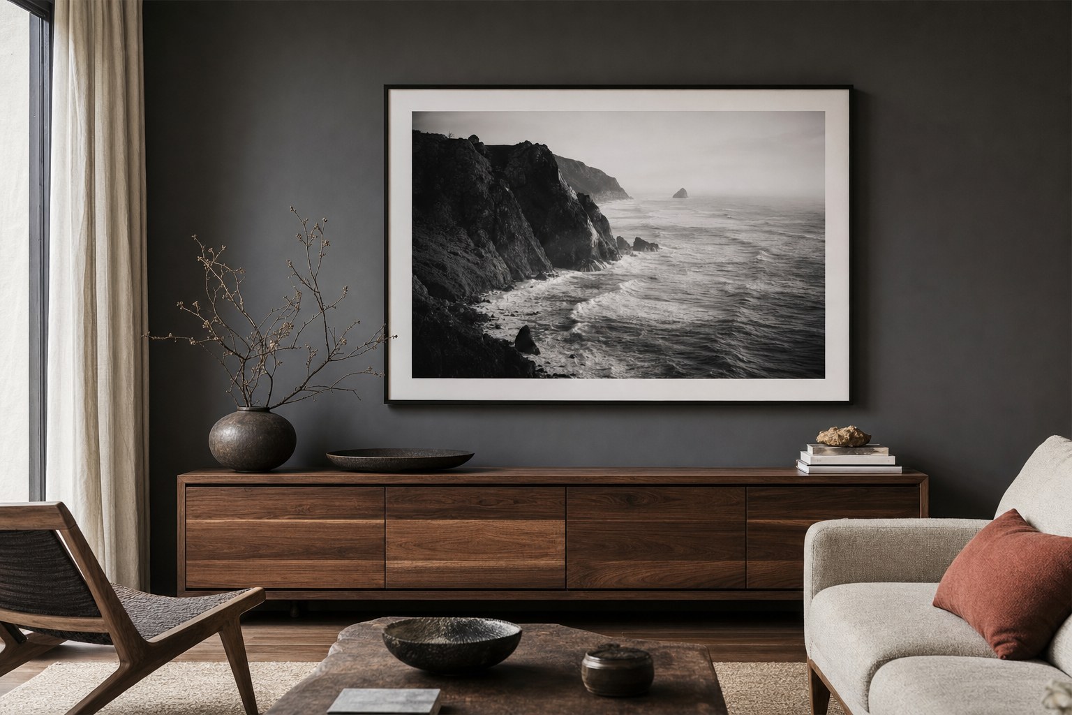 A large black-and-white coastal photograph displayed above a walnut console in a dark living room.