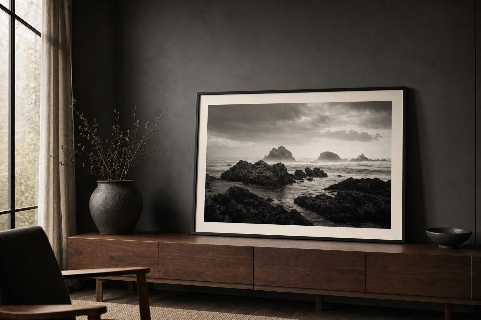 A framed black-and-white coastal landscape photograph on a walnut console in a quiet dark room.