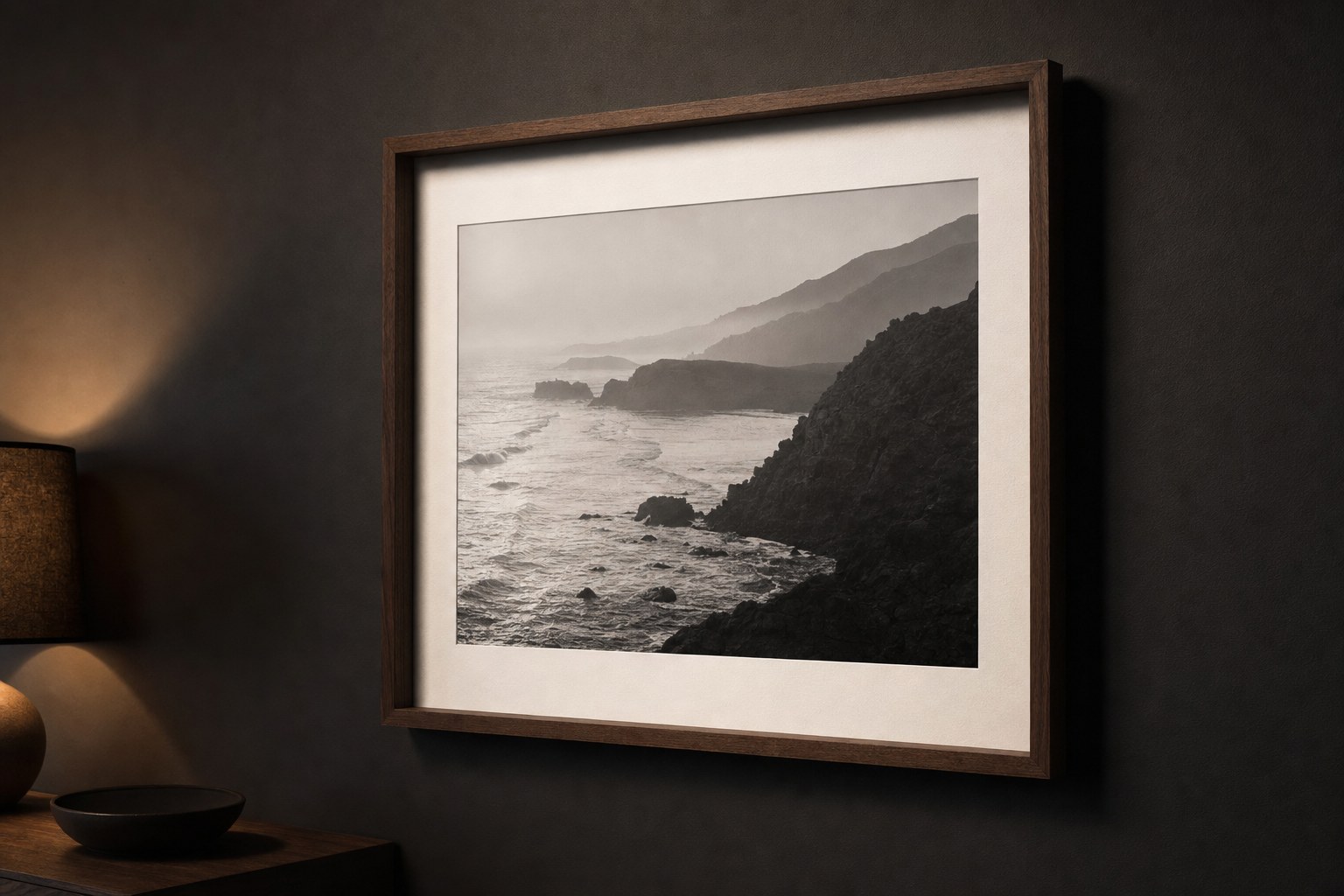 A framed coastal landscape photograph illuminated by a soft evening lamp.