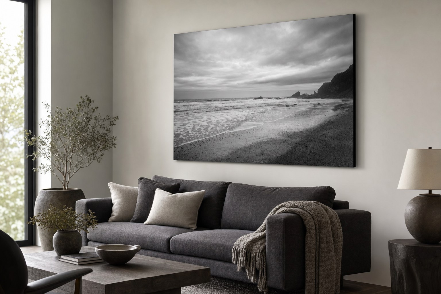 A large black-and-white shoreline photograph above a charcoal sofa.