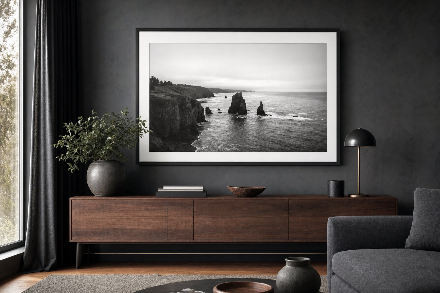 A framed black-and-white coastal photograph above a walnut console in a charcoal living room.