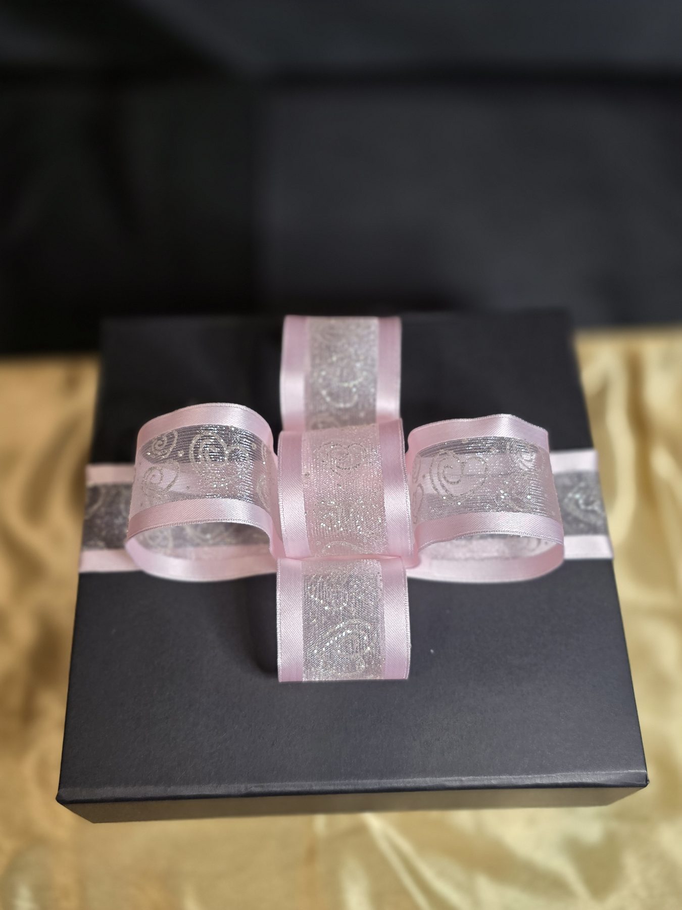 Black gift box finished with a pink and silver ribbon bow