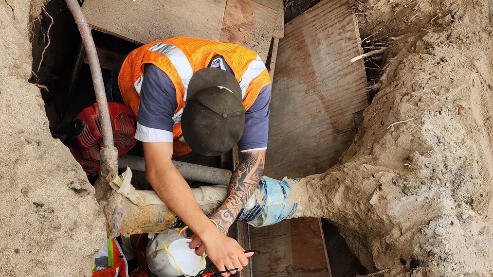 Technician working at exposed sewer piping in an excavation access pit