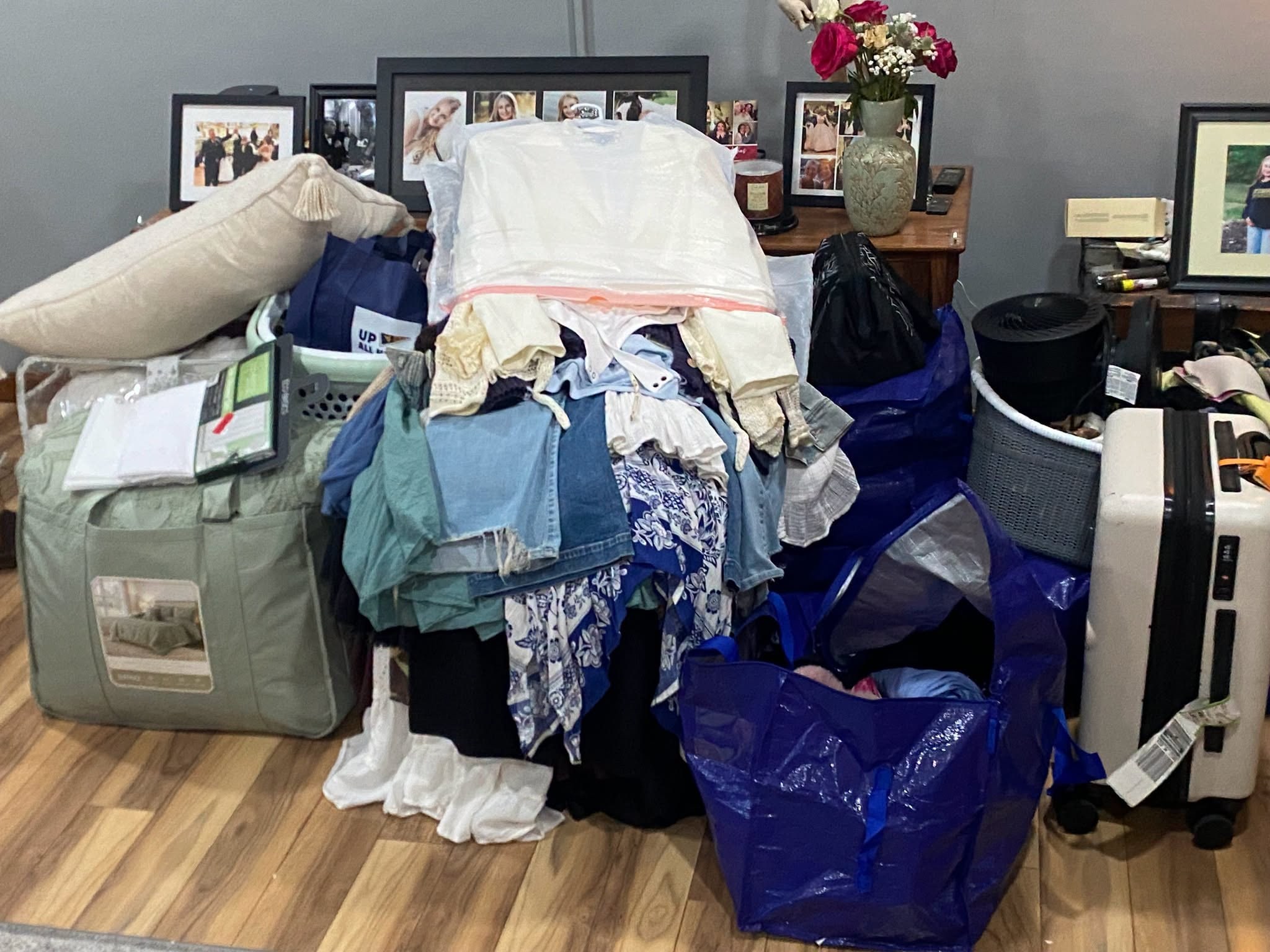 A bedroom piled with bags, bedding, clothes, and college move-in supplies.
