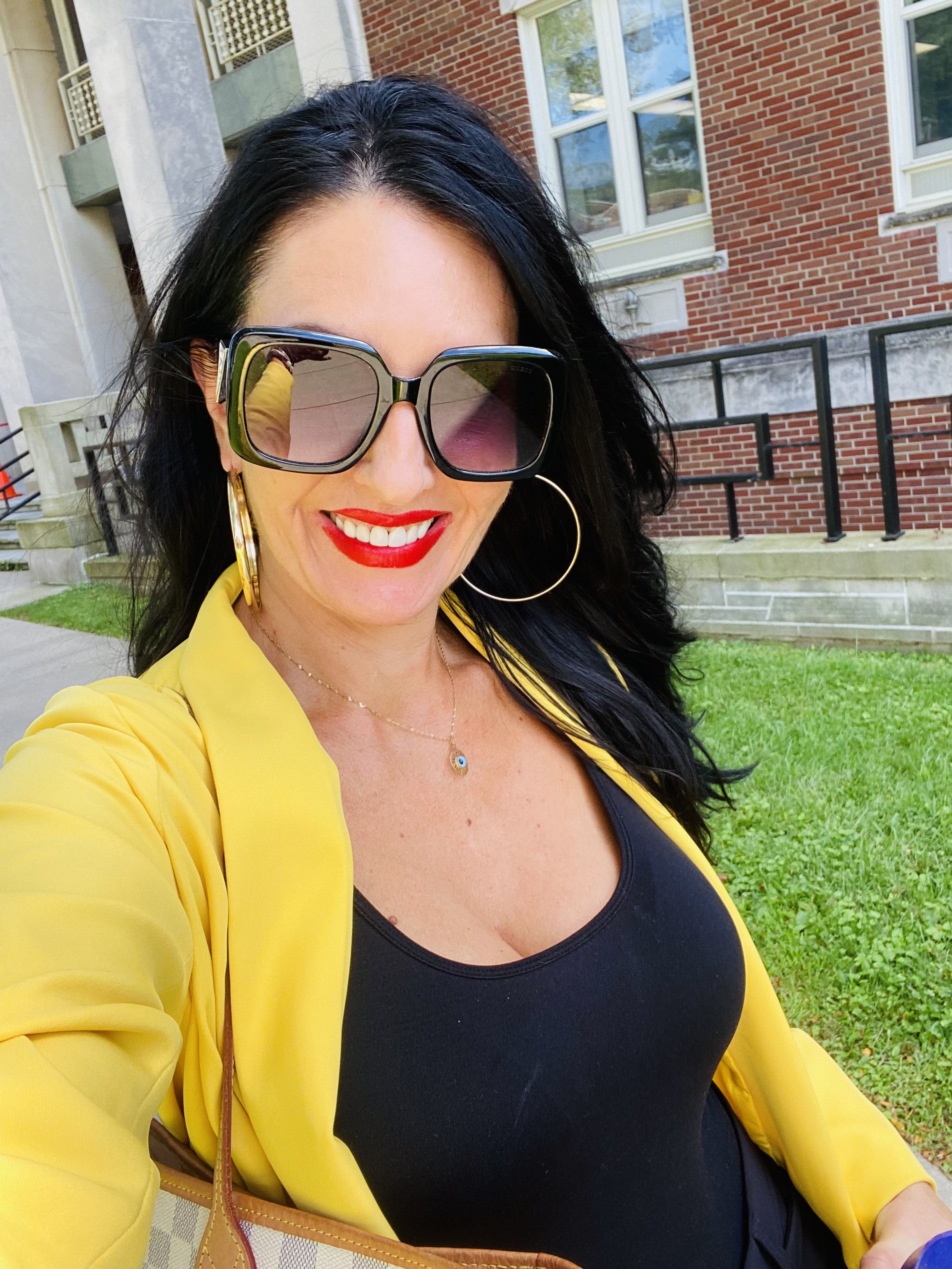 Stacey Creely smiling outside in a yellow blazer and sunglasses.