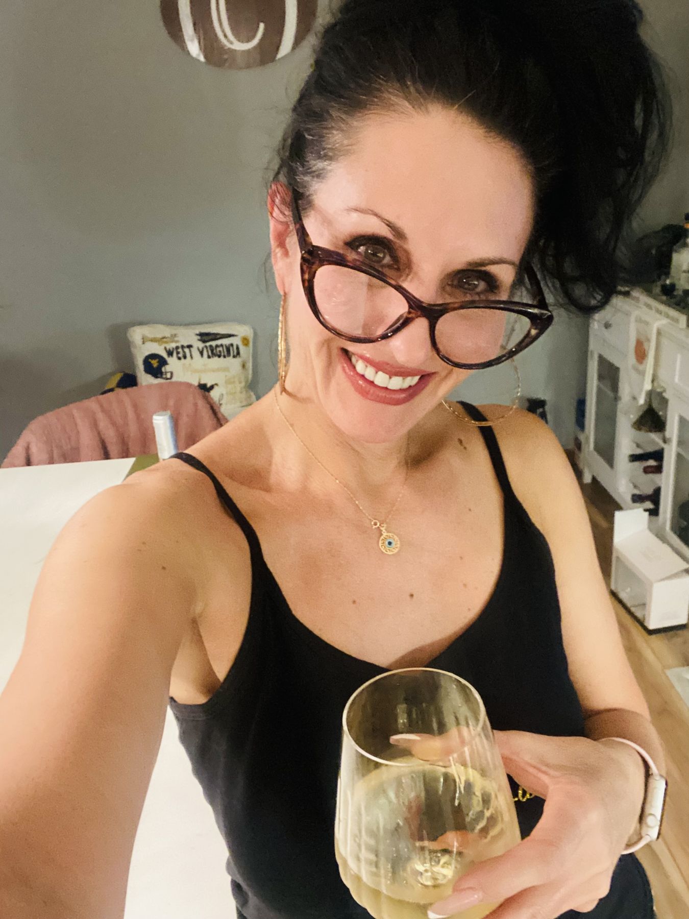 Stacey smiling in glasses and holding a glass of white wine at home.